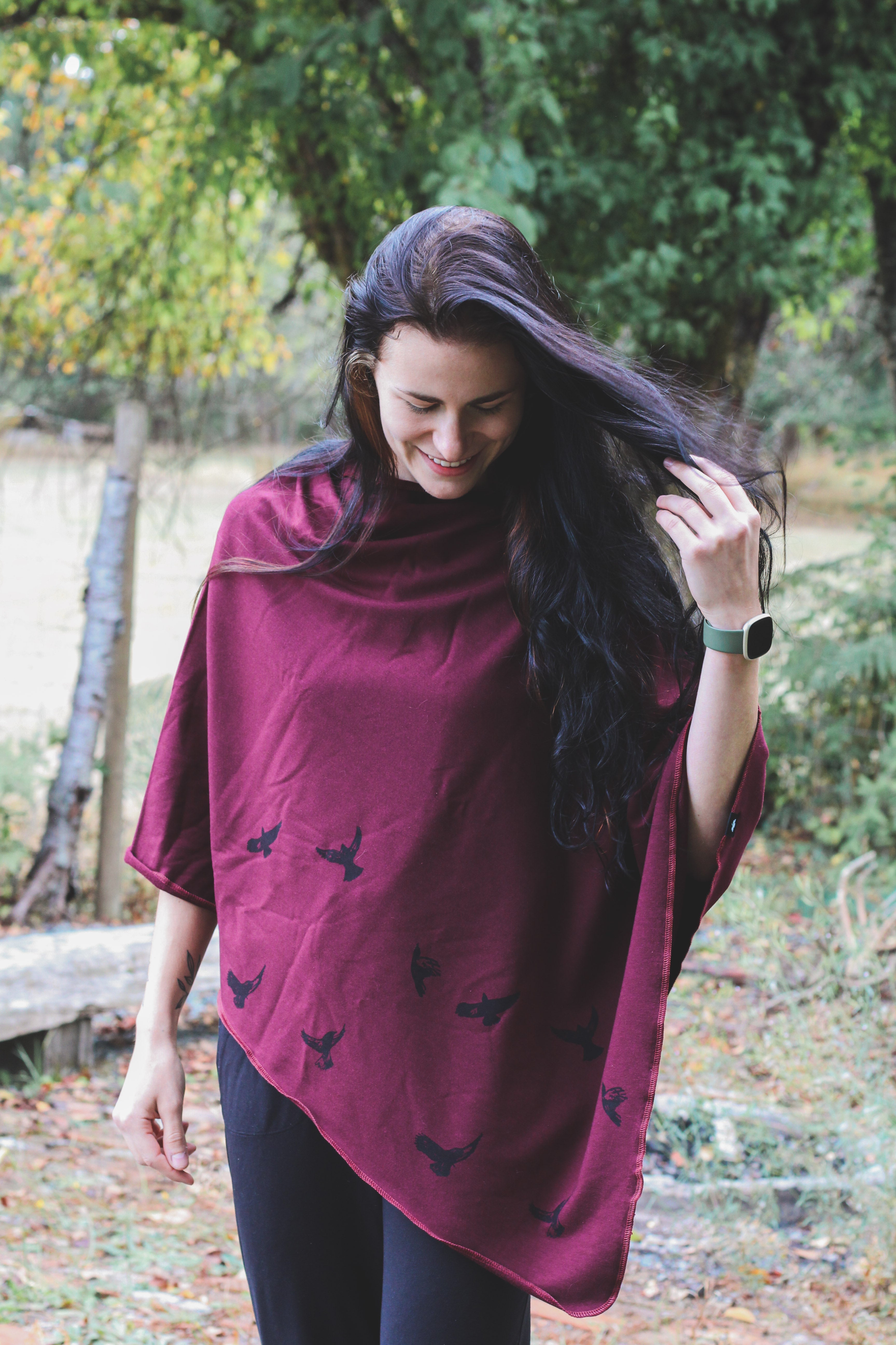 Woman wearing a burgundy poncho with black bird patterns in an outdoor setting.