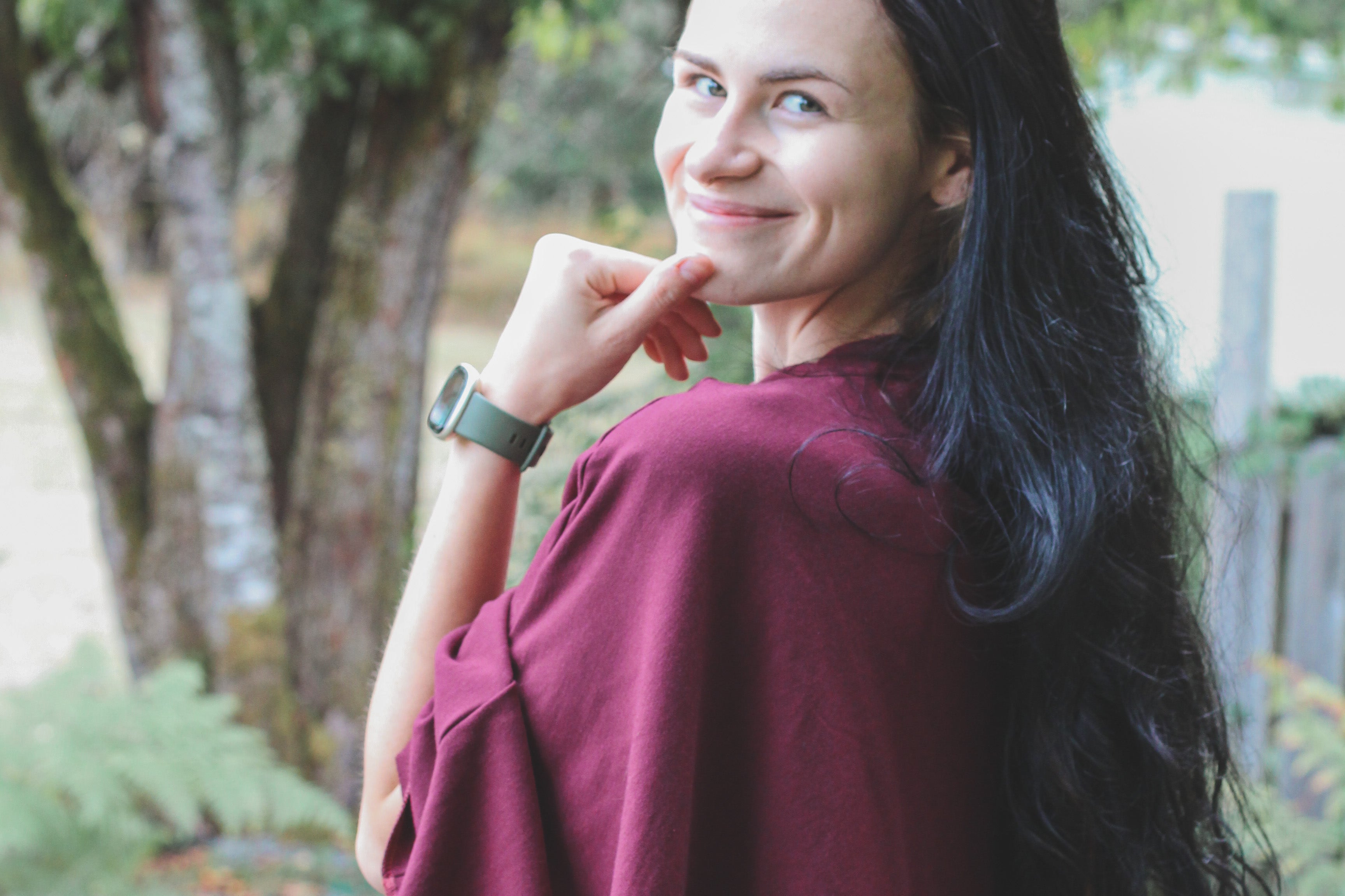Woman in a burgundy sweater standing outdoors with trees in the background