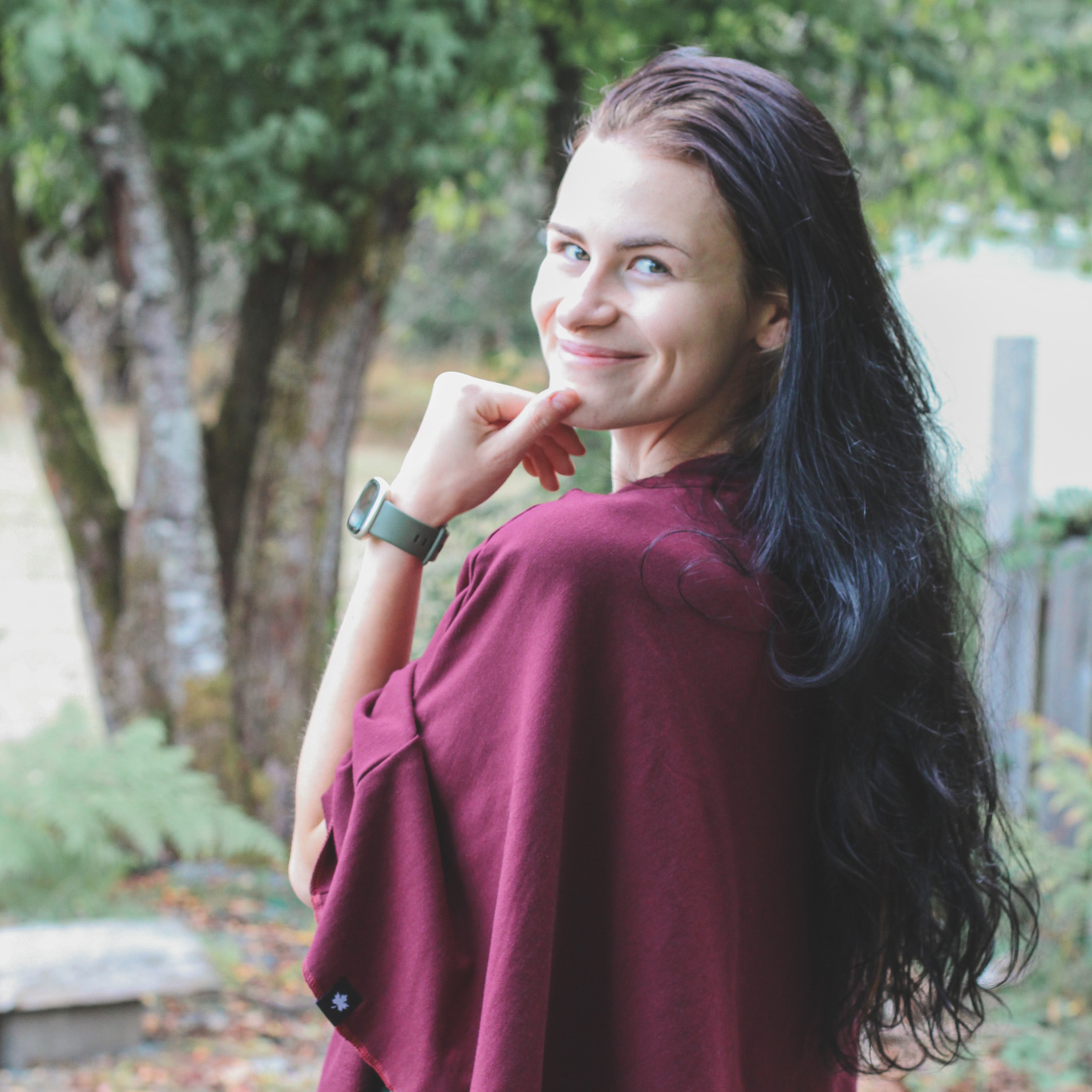 Woman in a burgundy sweater standing outdoors with trees in the background