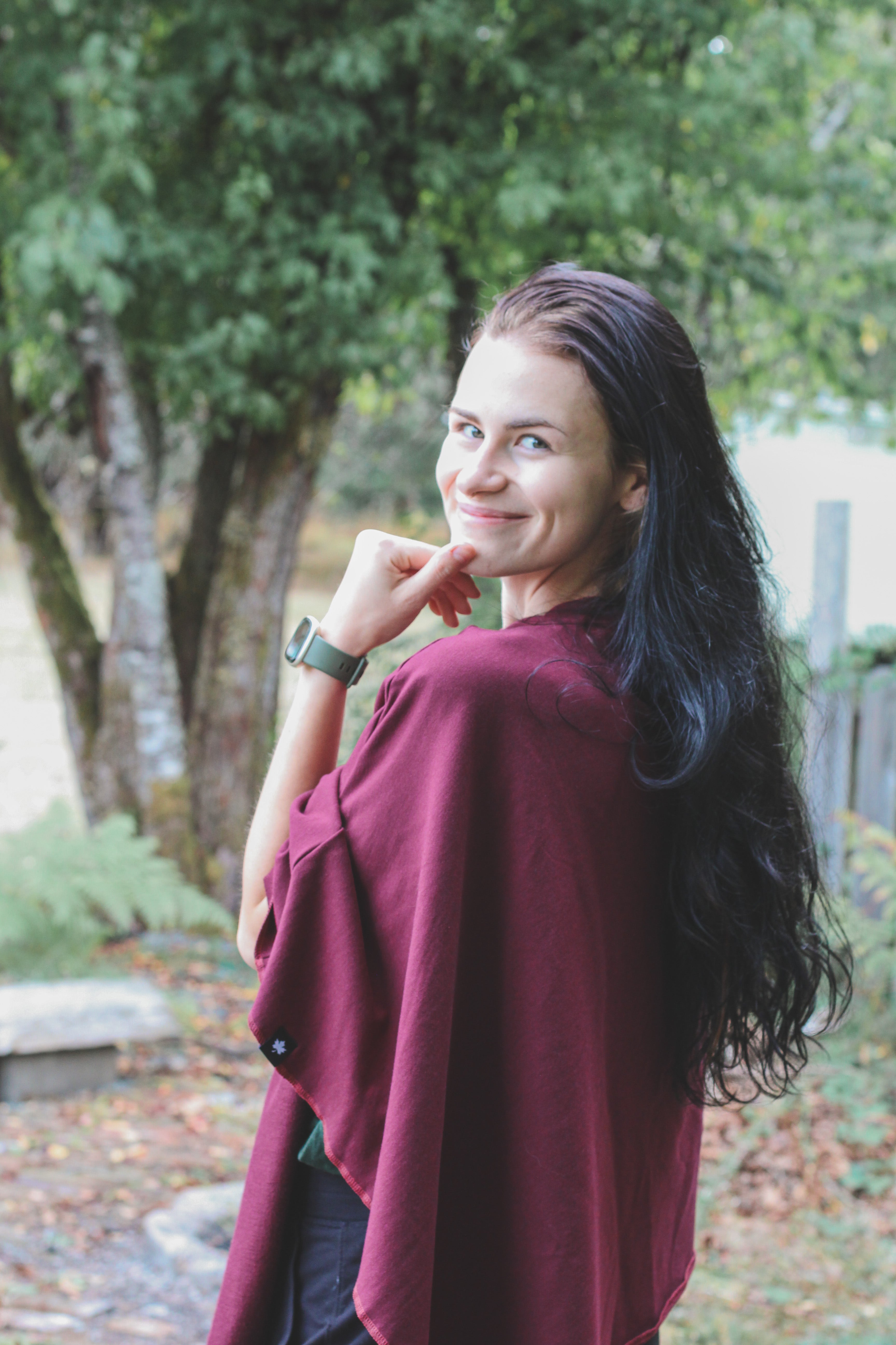 Woman in a burgundy sweater standing outdoors with trees in the background
