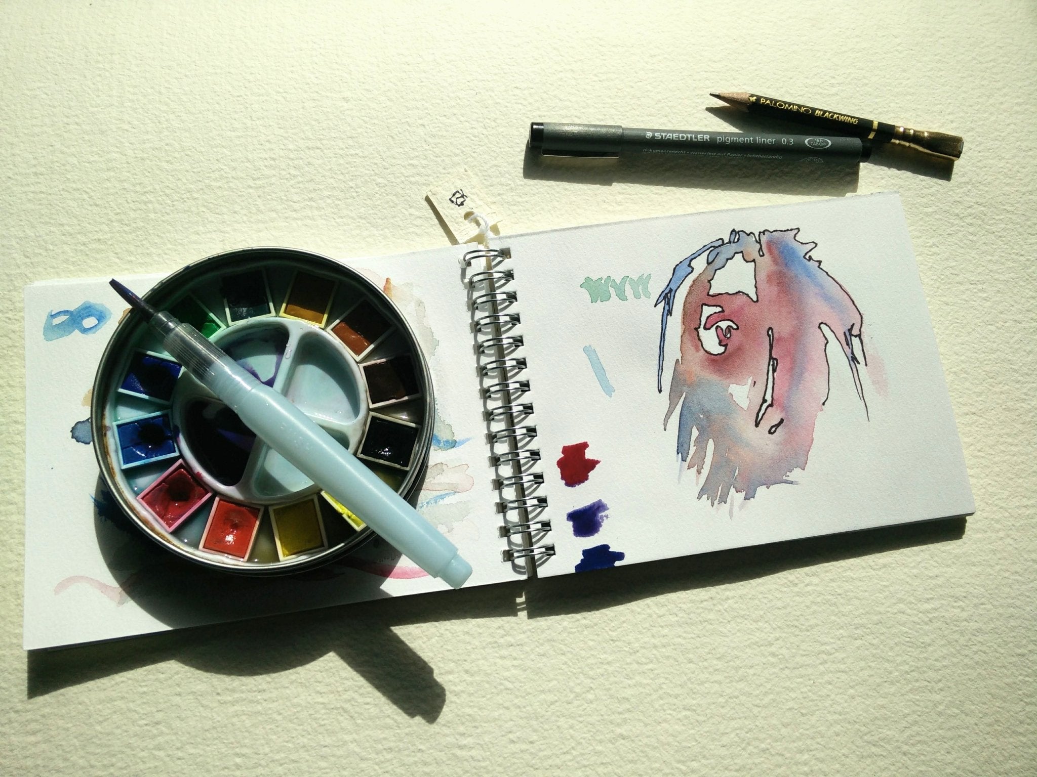 Artistic setup with watercolor palette, brush, and drawing on a notebook