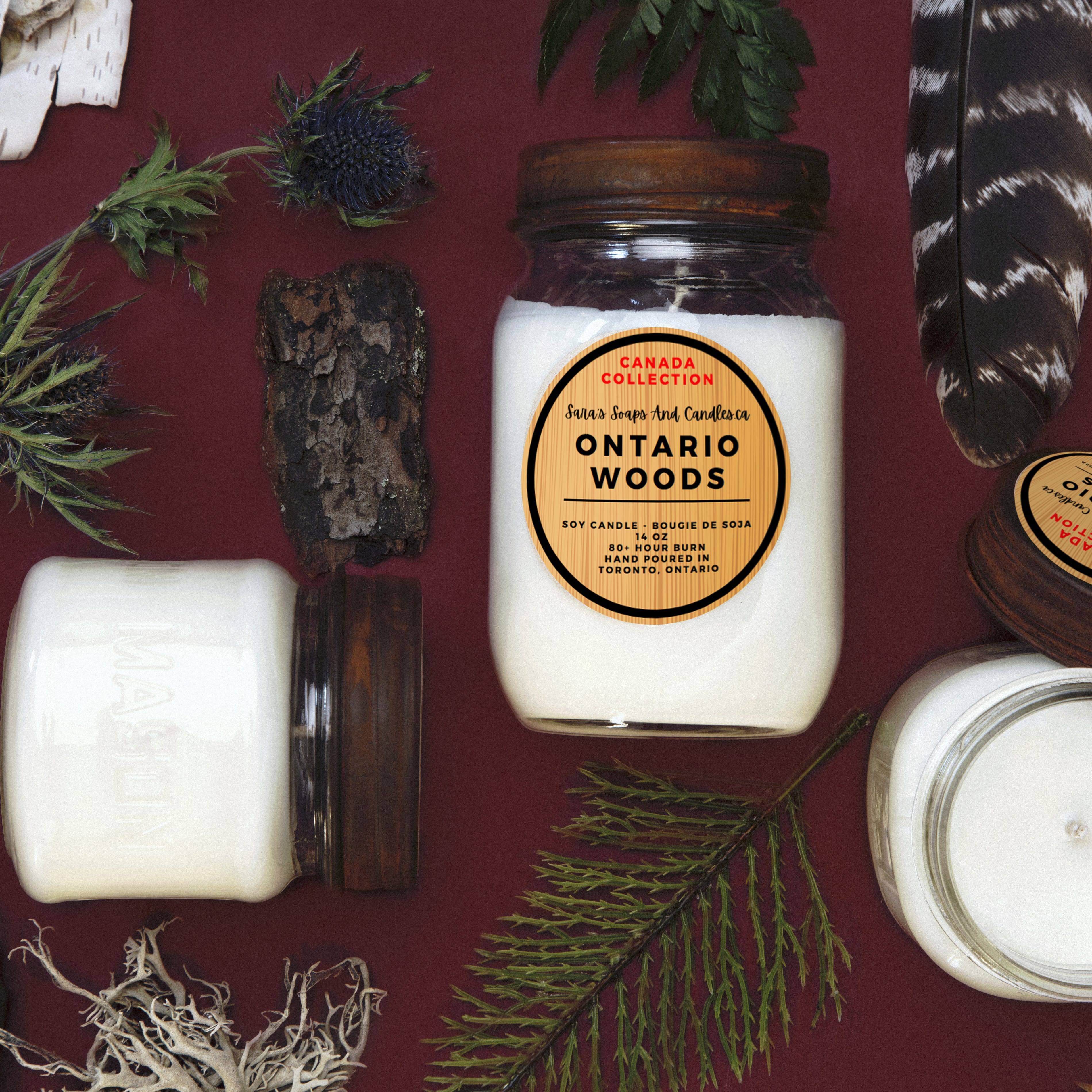 Candle jar labeled 'Ontario Woods' surrounded by natural elements on a red background