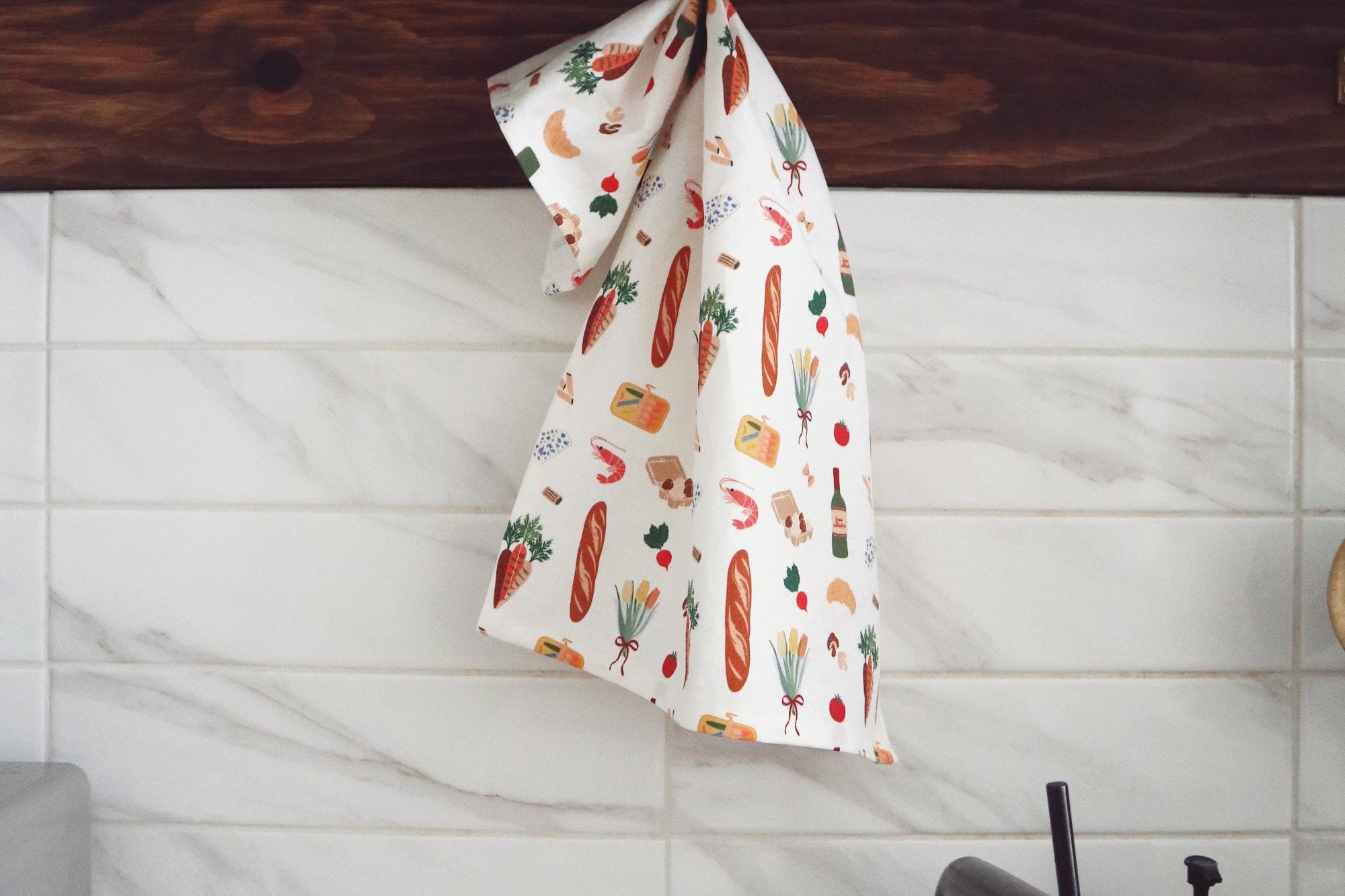 Kitchen setting with a towel featuring food illustrations hanging over a wooden shelf.