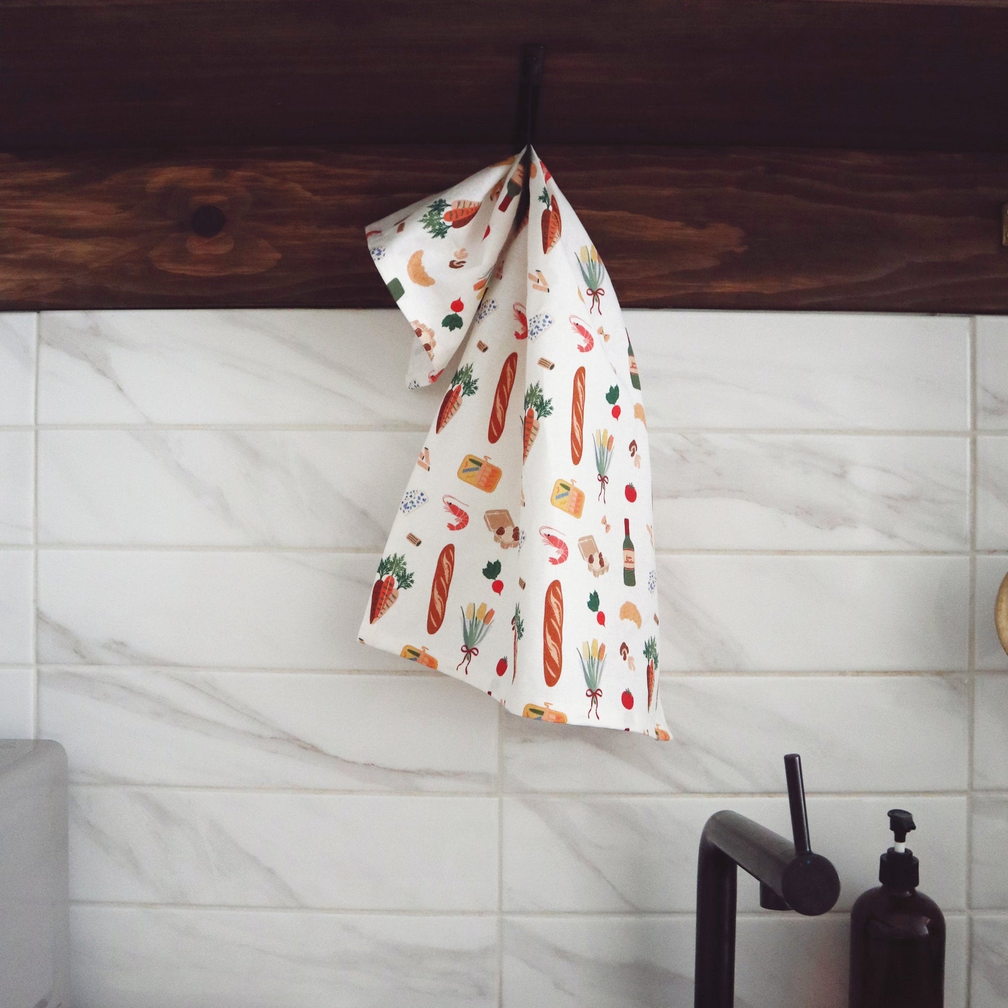 Kitchen setting with a towel featuring food illustrations hanging over a wooden shelf.