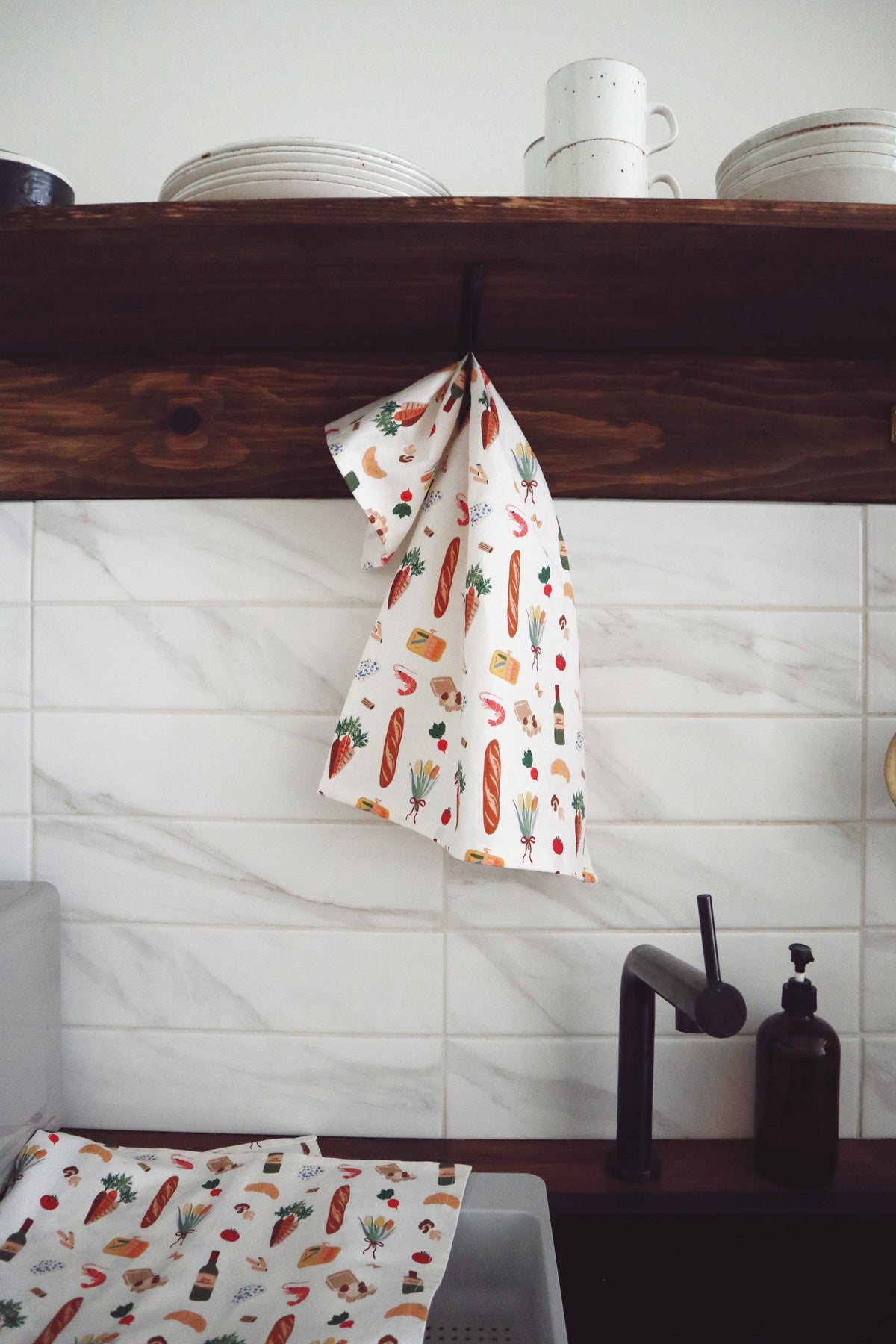 Kitchen setting with a towel featuring food illustrations hanging over a wooden shelf.