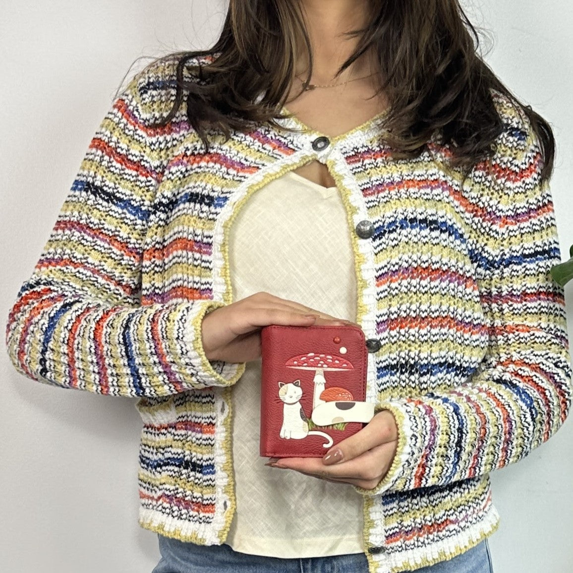 Person wearing a colorful striped jacket holding a Espe Vegan Corp red wallet with a cat design.