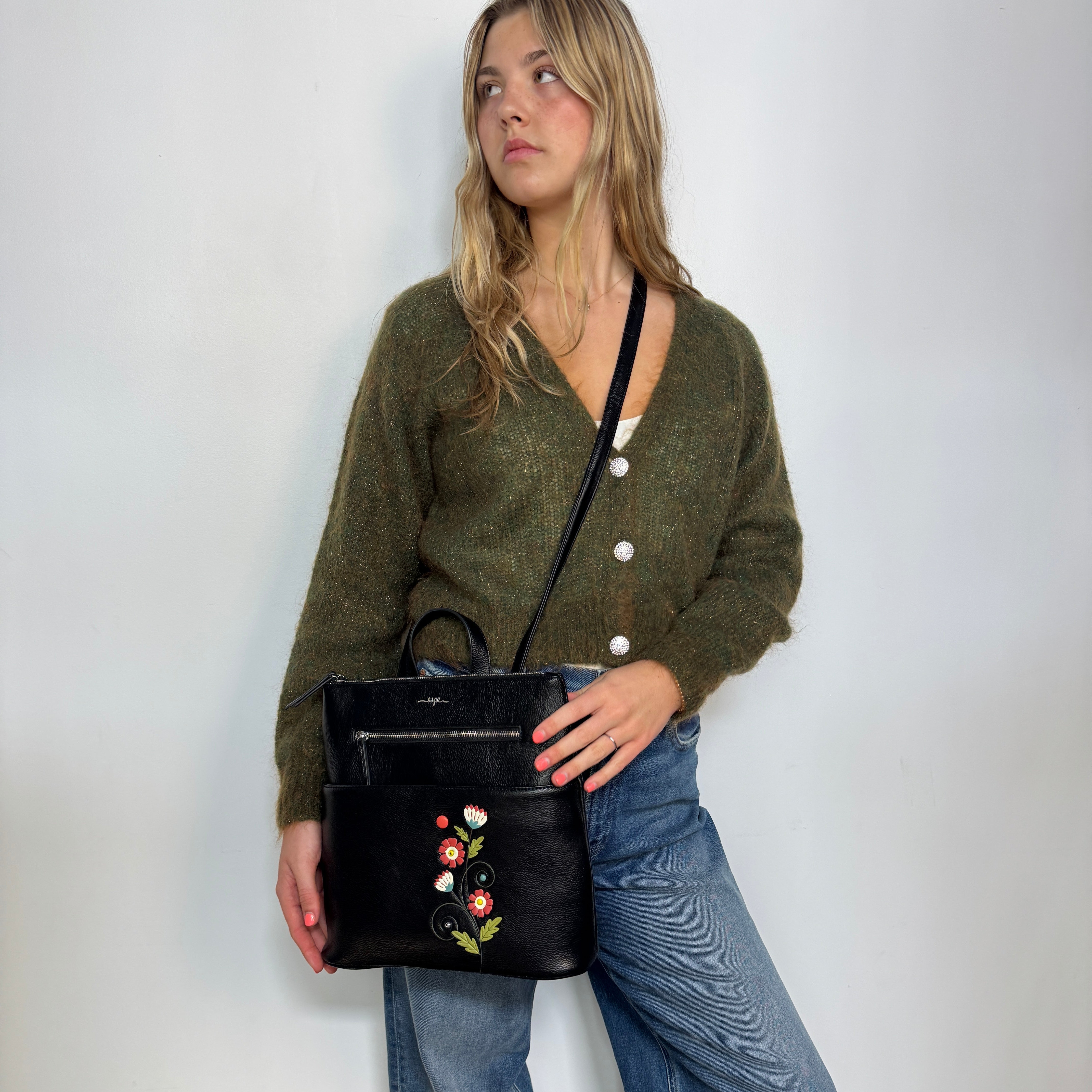 Woman holding a Espe Vegan Corp black handbag with floral embroidery against a plain background