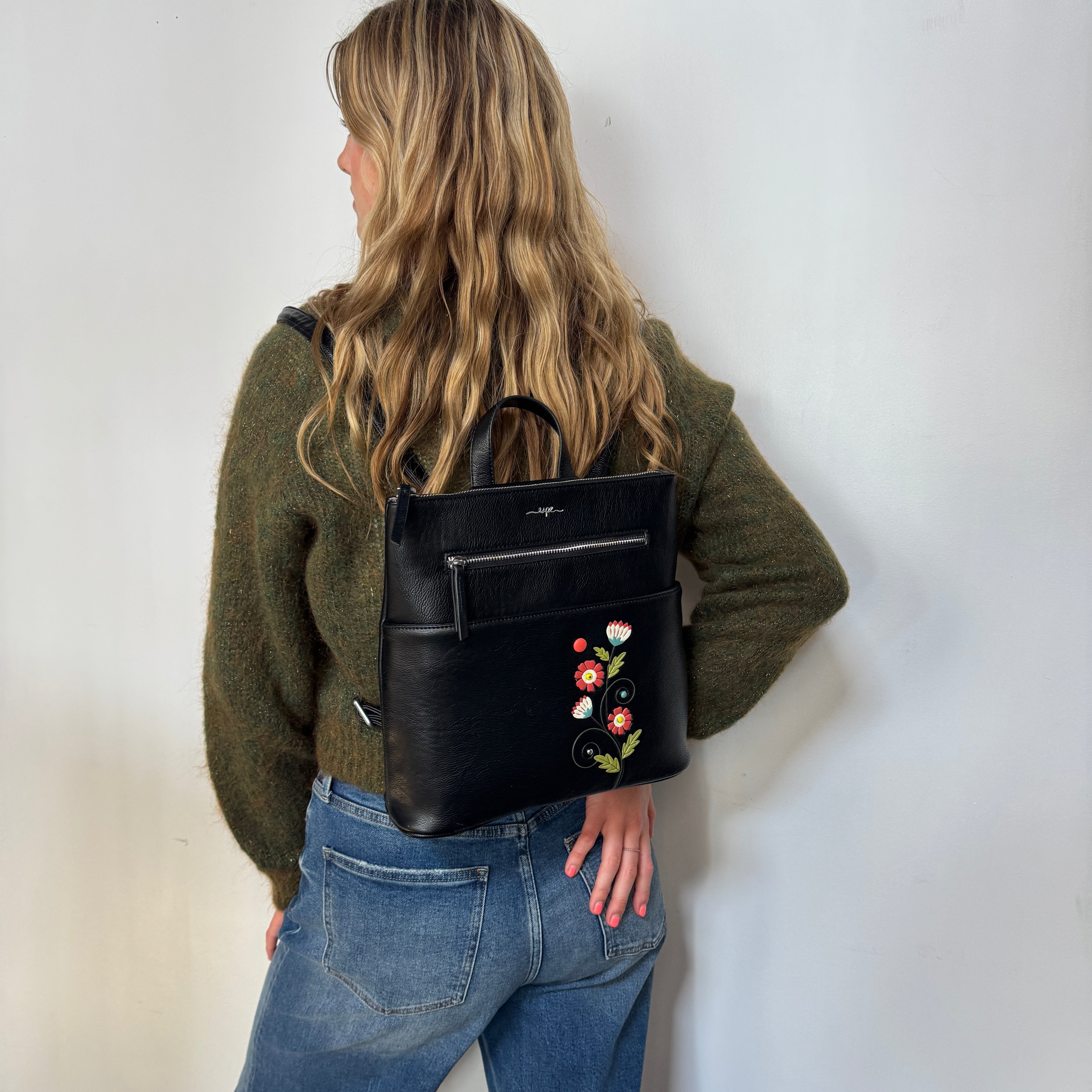 Person wearing a Espe Vegan Corp black backpack with floral embroidery against a white background