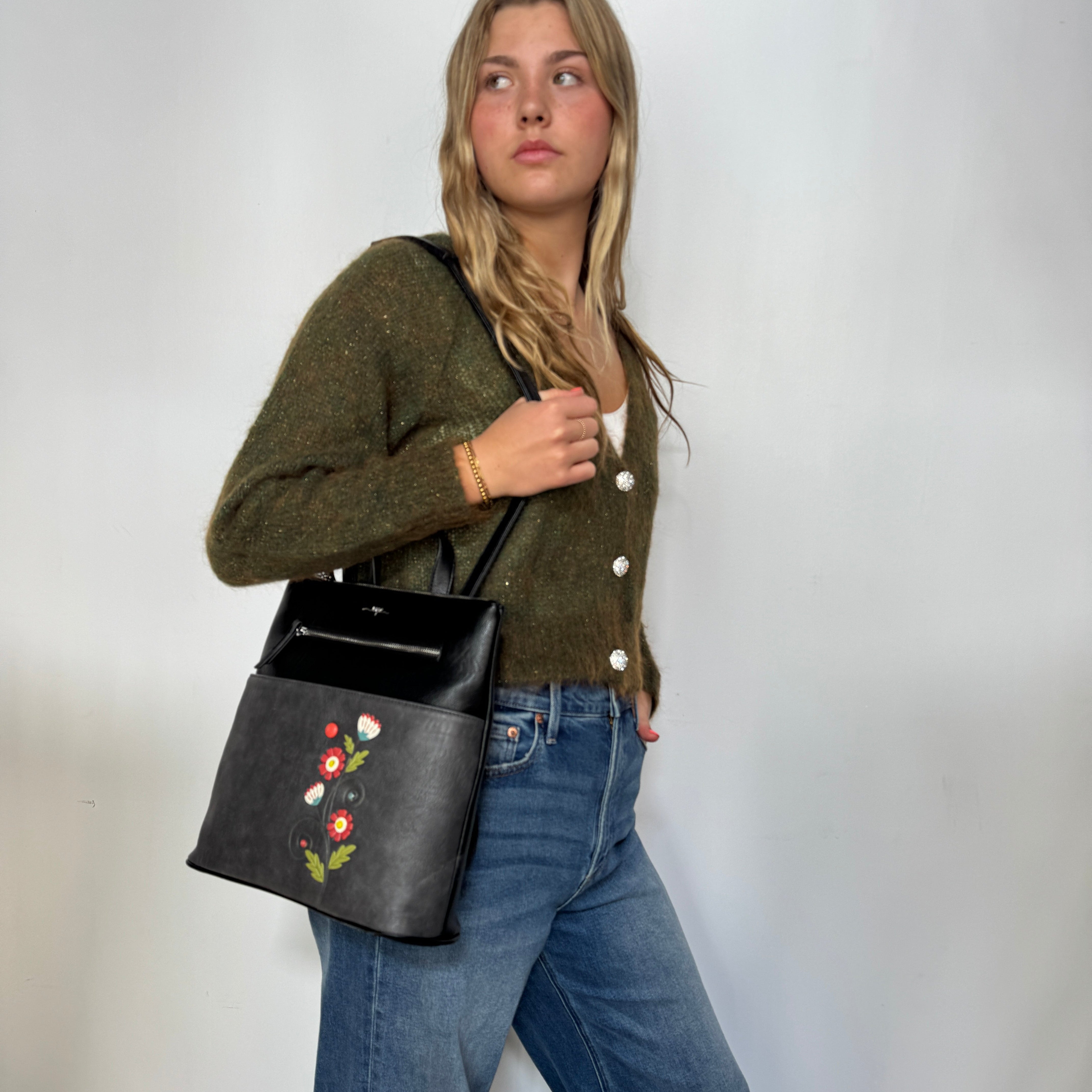 Woman holding a Espe Vegan Corp black handbag with floral embroidery against a plain background