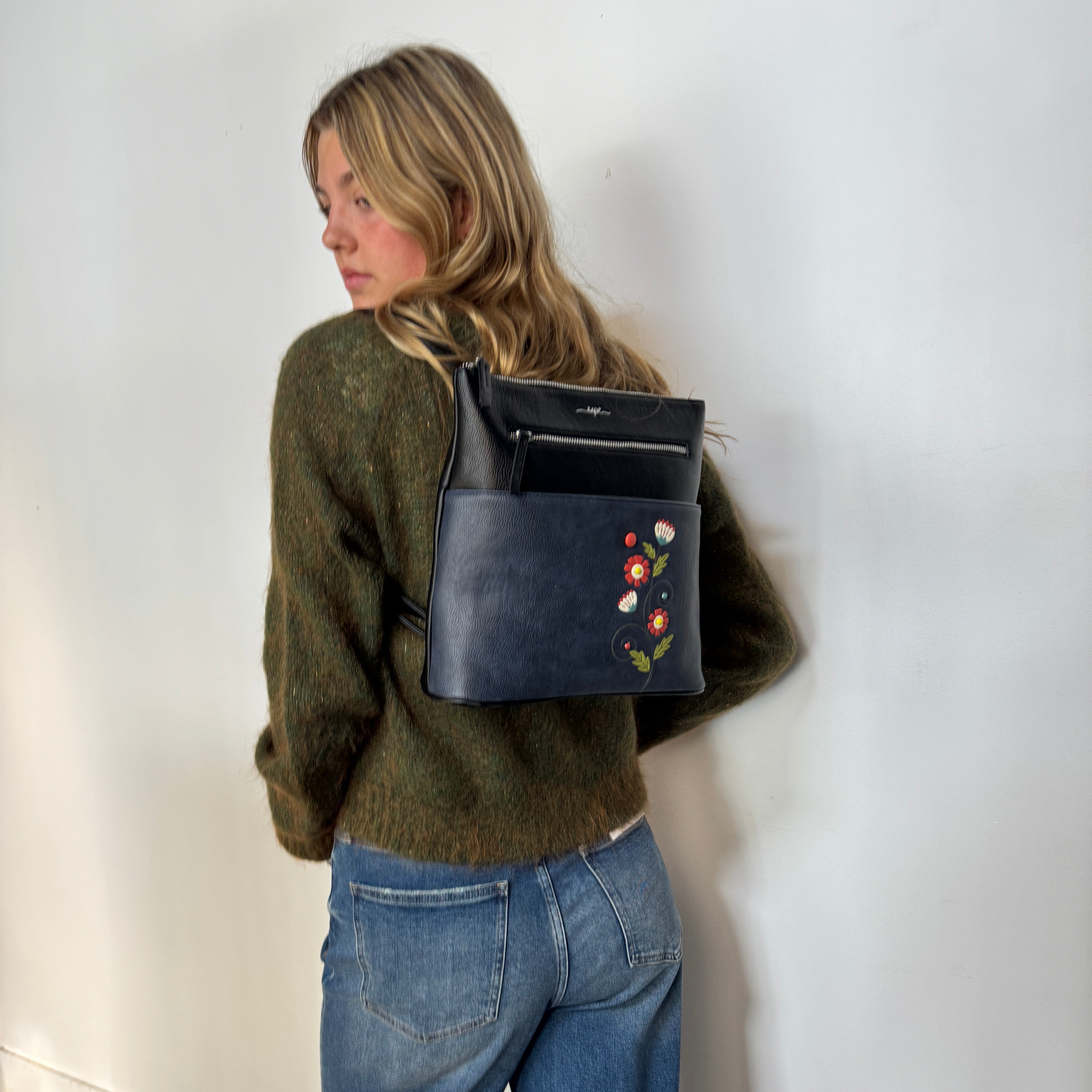 Person wearing a Espe Vegan Corp black leather bag featuring floral embroidery on a white background