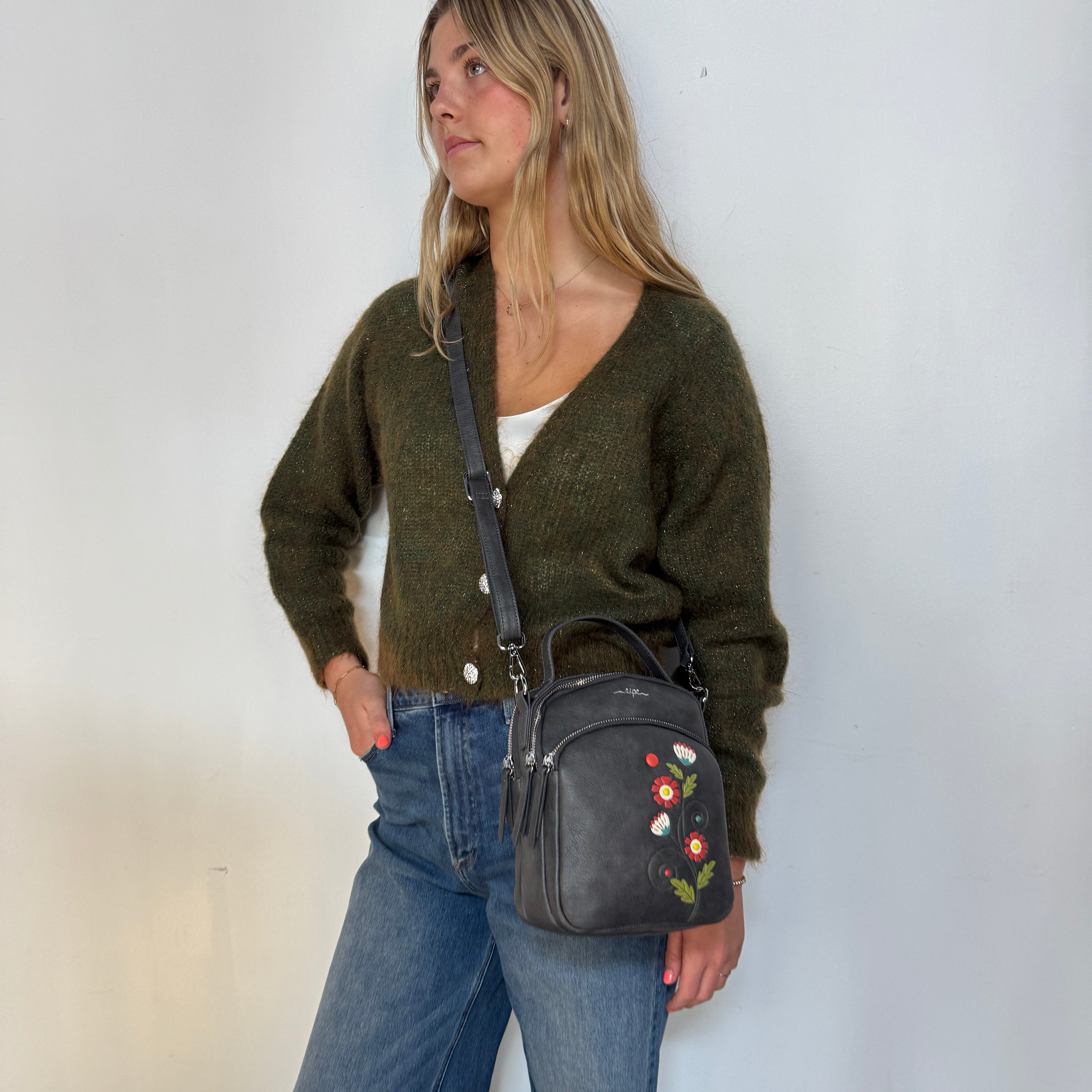 Woman holding a Espe Vegan Corp black handbag with floral embroidery against a white wall