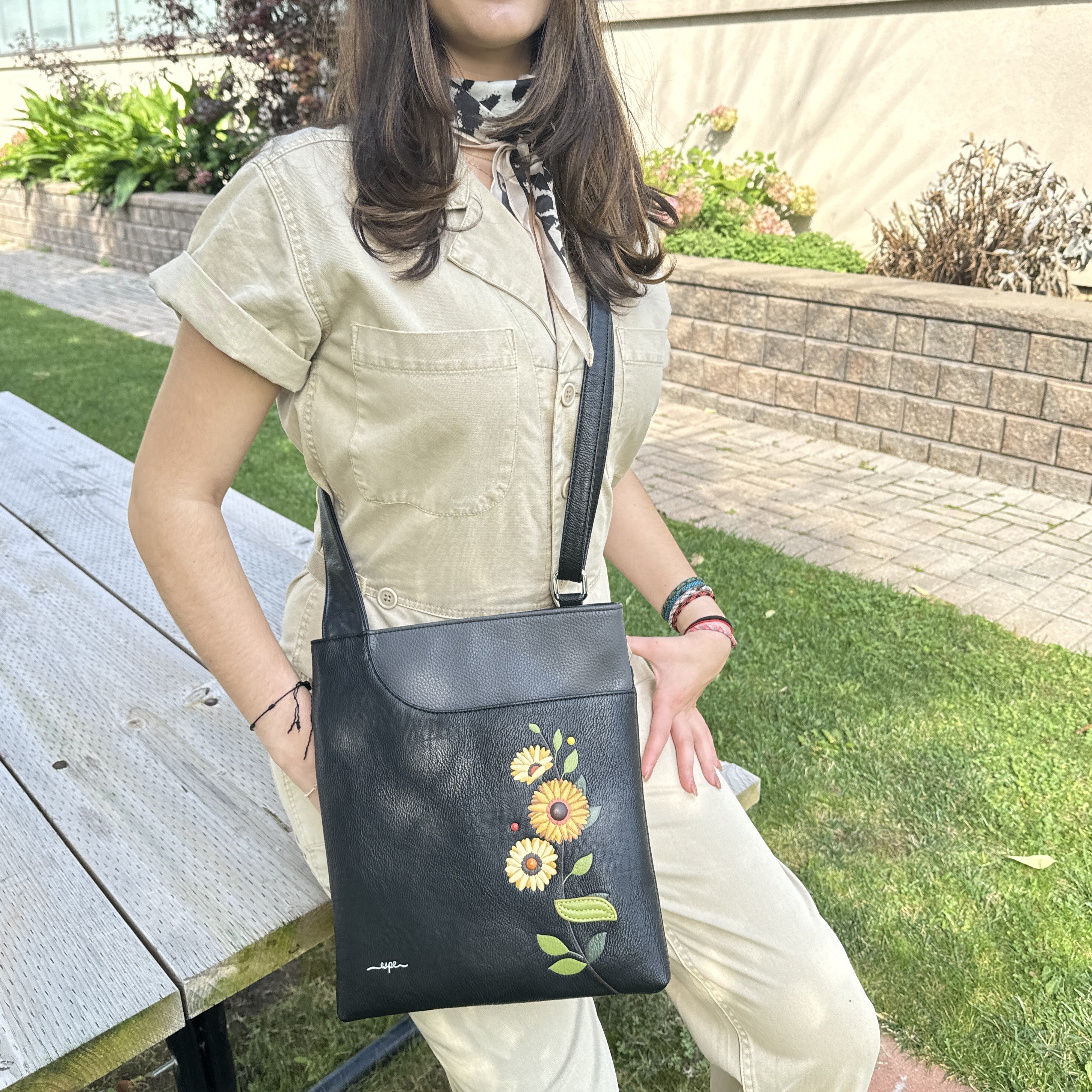 Person holding a black handbag with floral designs outdoors Espe Vegan Corp 