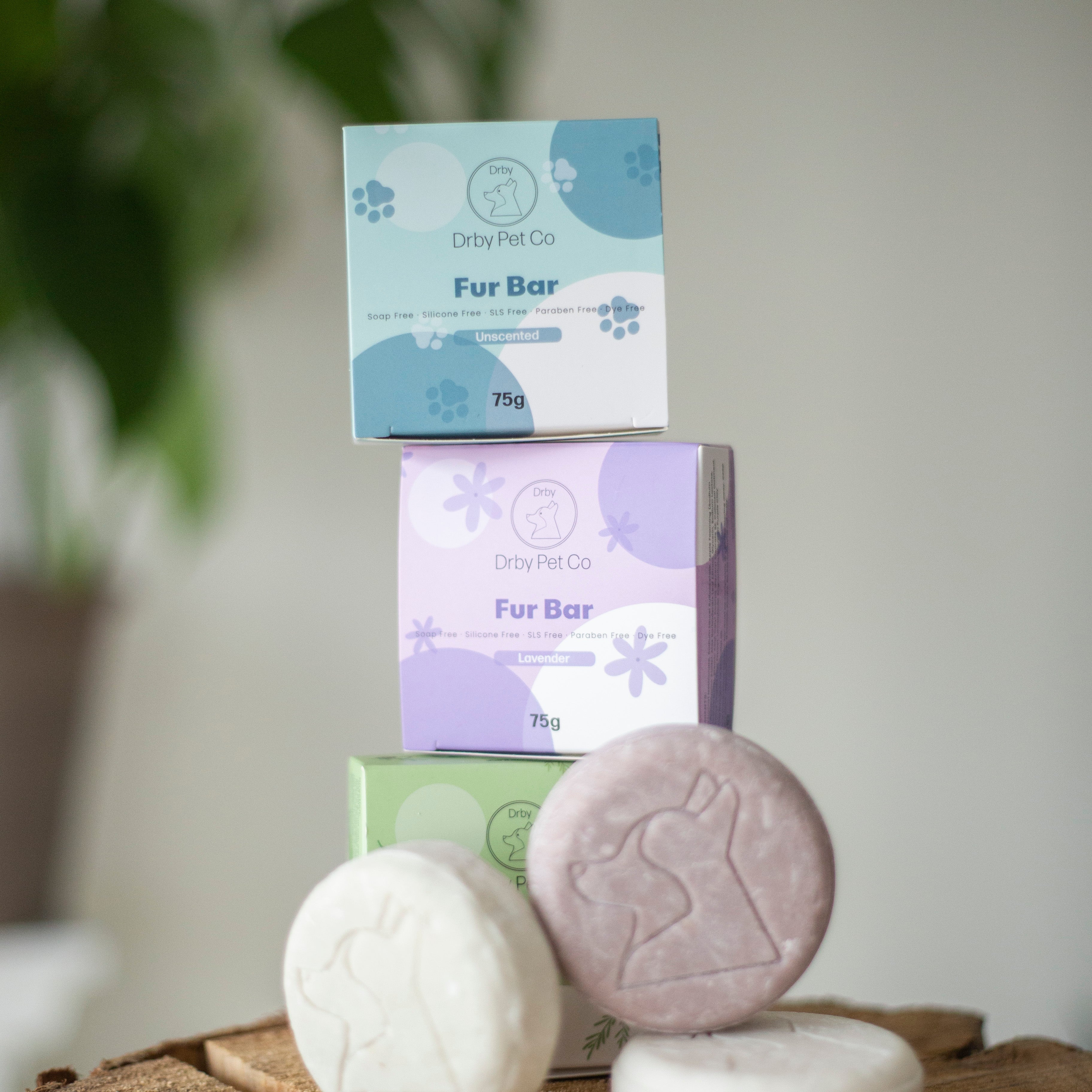 Pet care products including bath bars and boxes on a wooden surface with a blurred plant background.