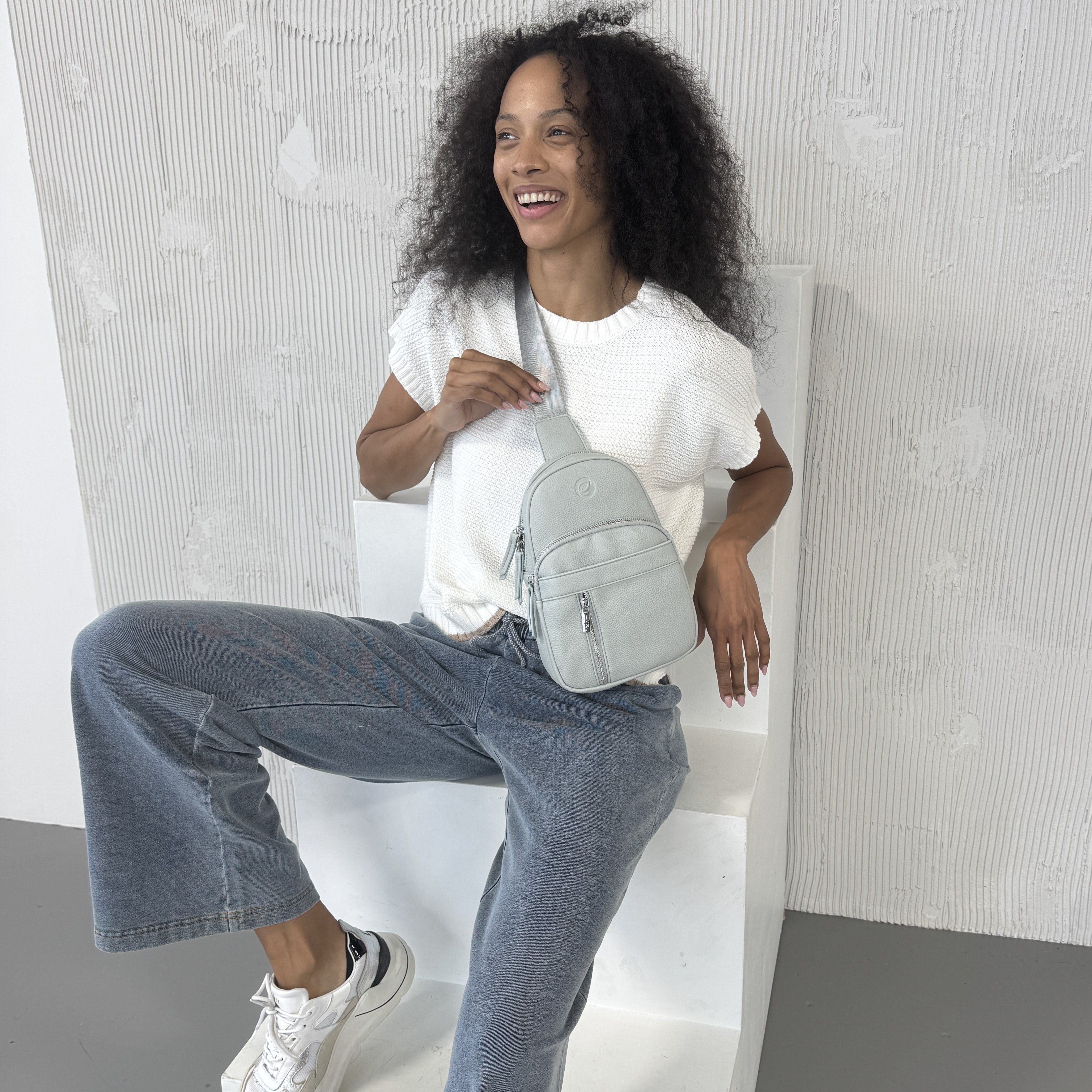 Woman sitting on a white chair holding a Espe Vegan Corp grey backpack 