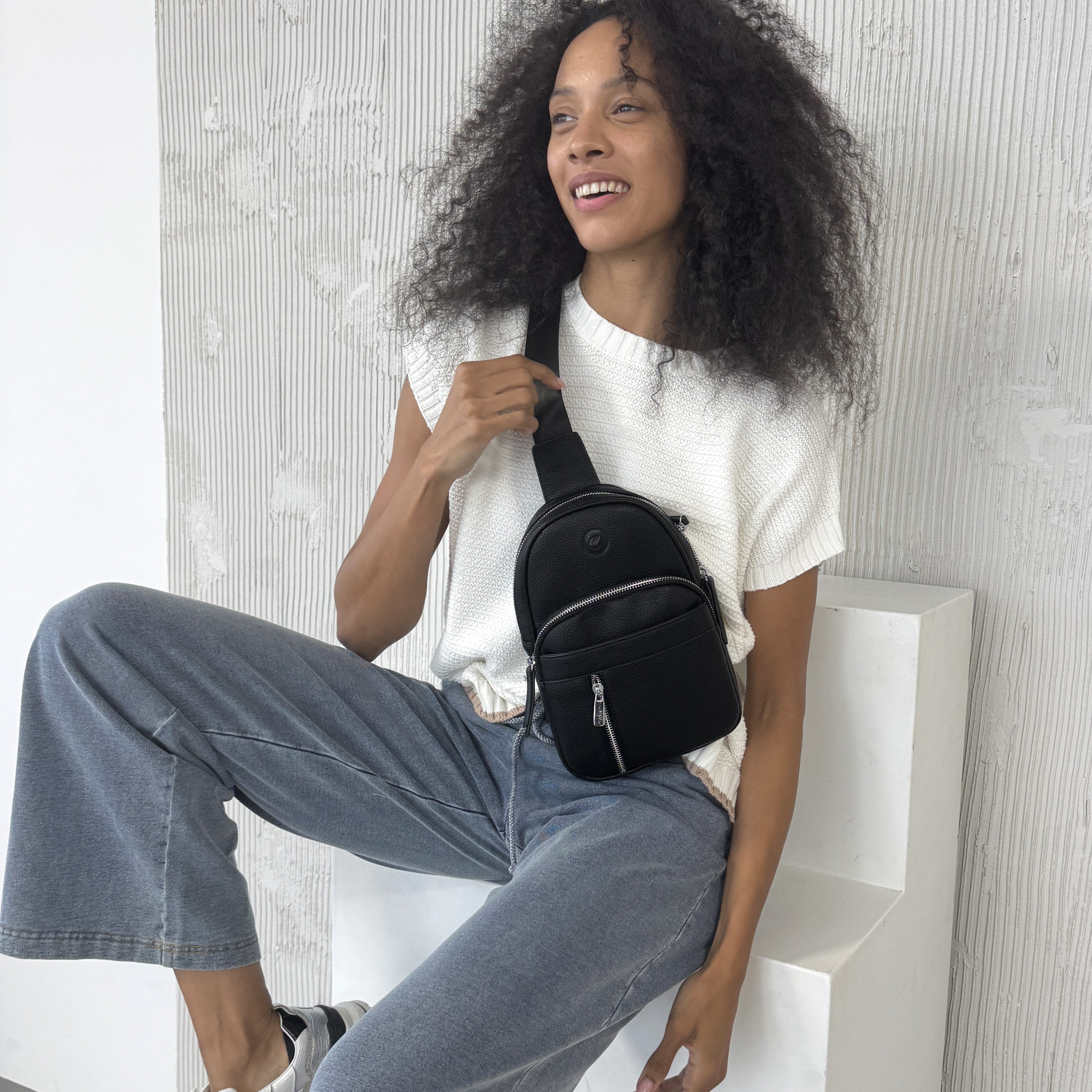 Woman sitting on a white chair holding a Espe Vegan Corp  black bag 