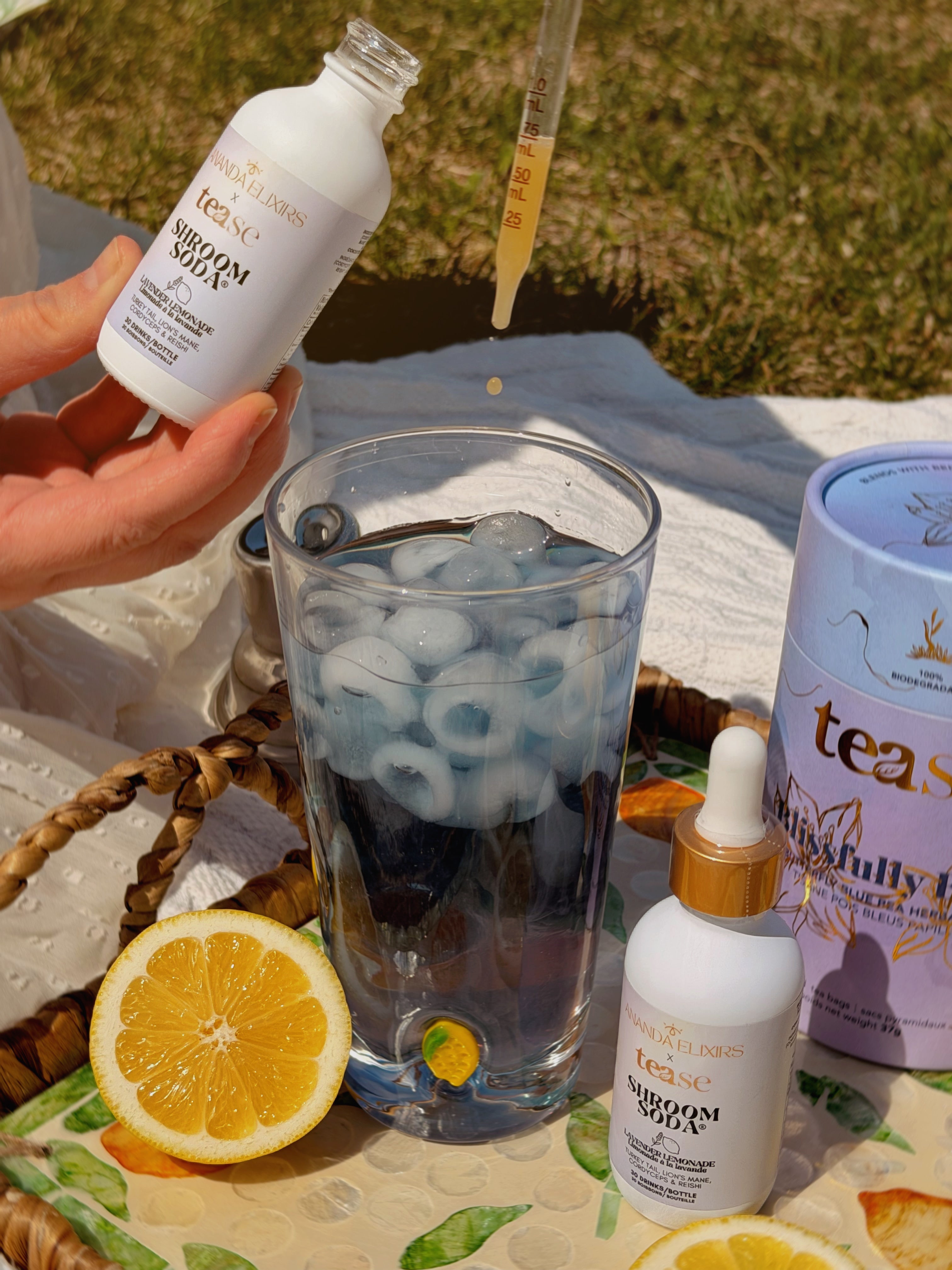 Ananda Elixirs Shroom Soda® – Lavender Lemonade – Person dropping Shroom Soda into iced blue mocktail outdoors with Tease tea canister