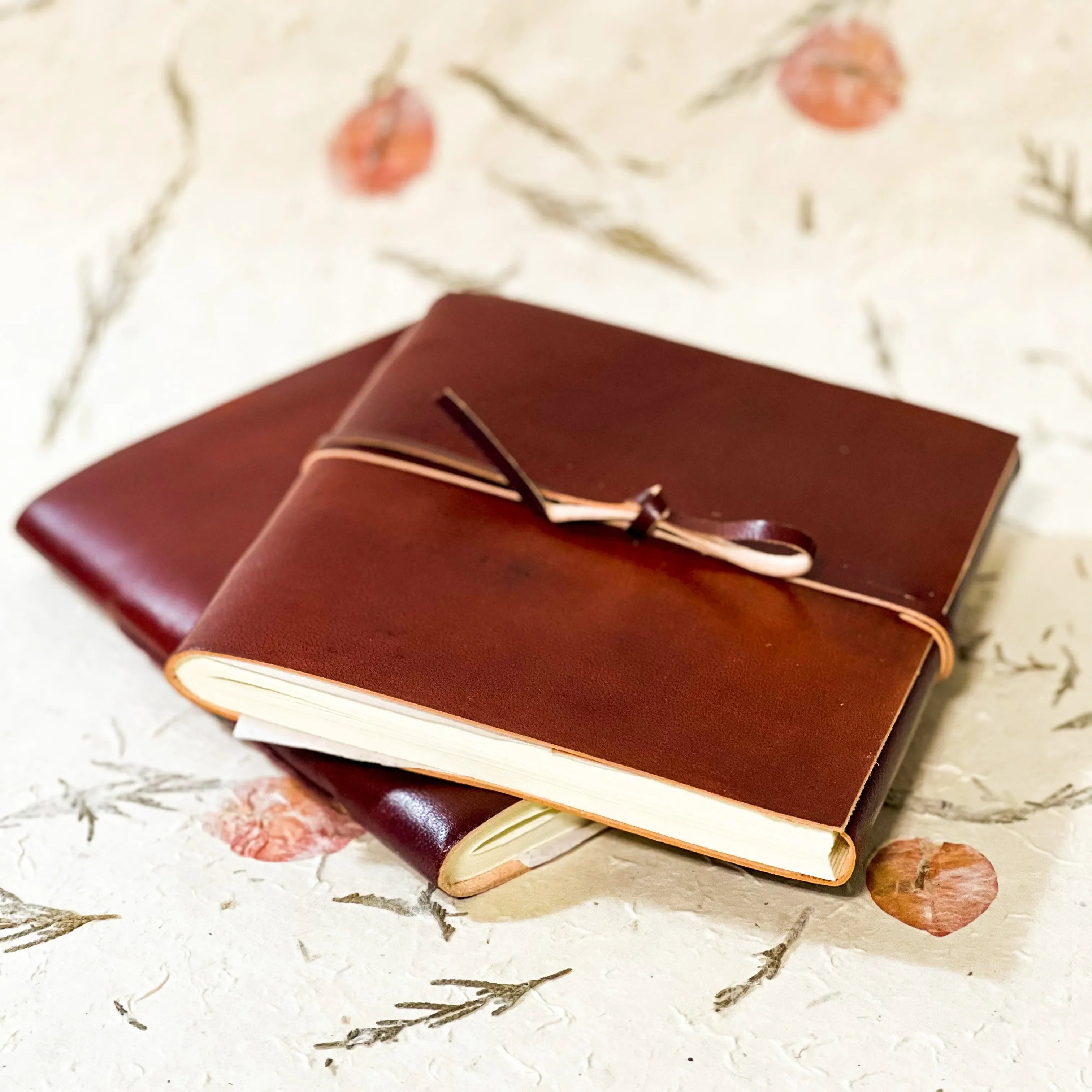 Two brown leather journals on a textured surface with floral patterns