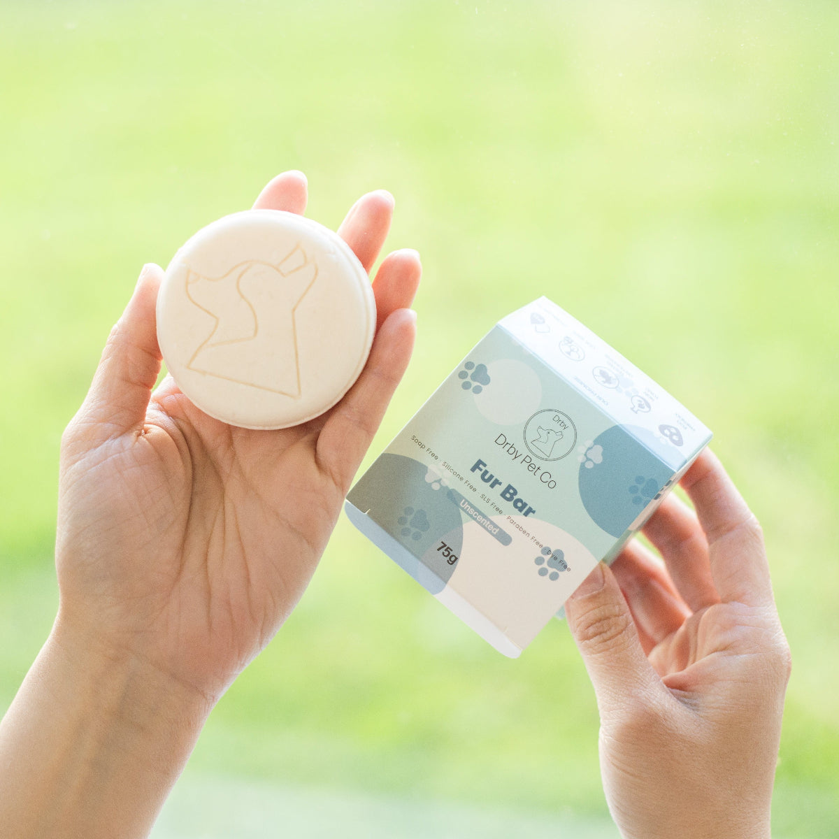Person holding a bath bomb and its packaging against a blurred green outdoor background