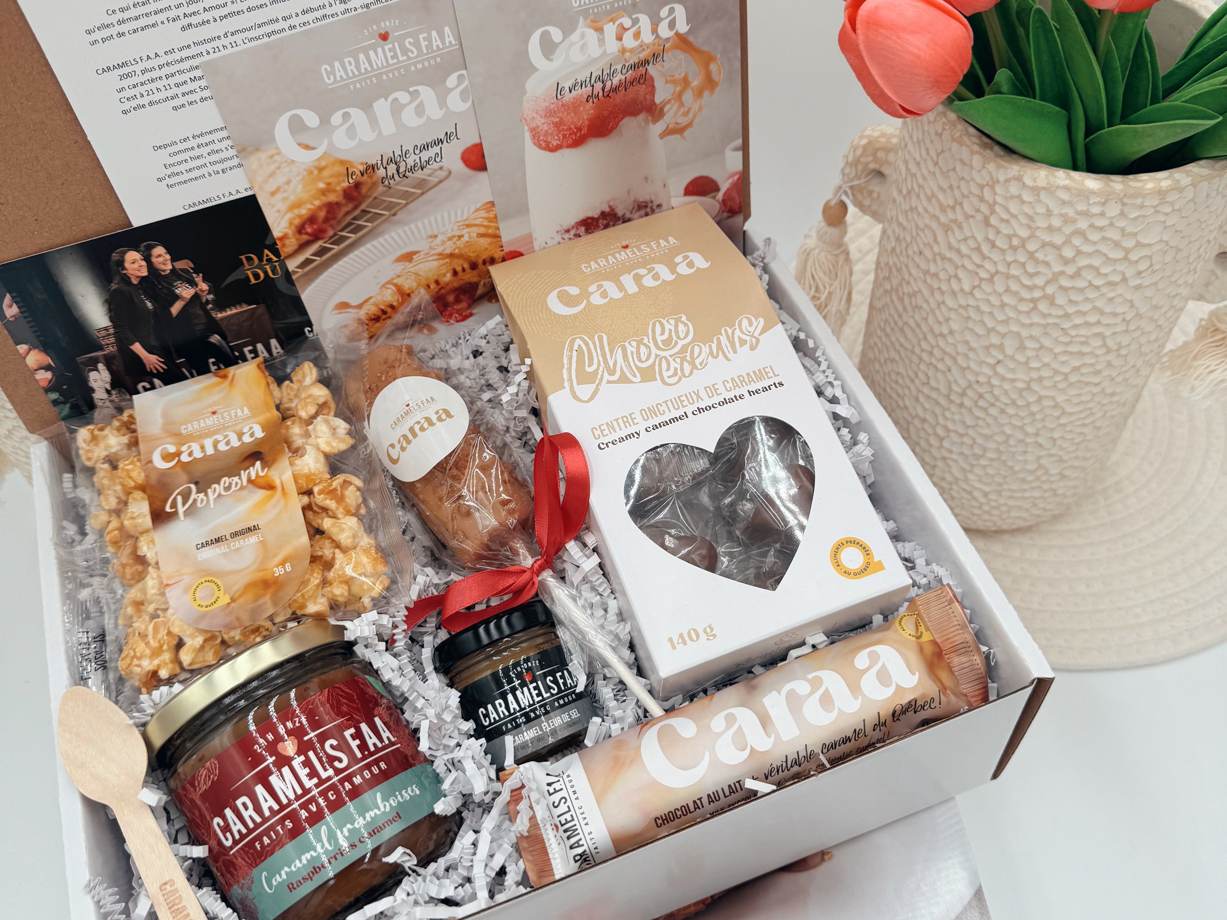 Gift box with Cama products including cheese, jam, and other snacks, accompanied by a vase of tulips.