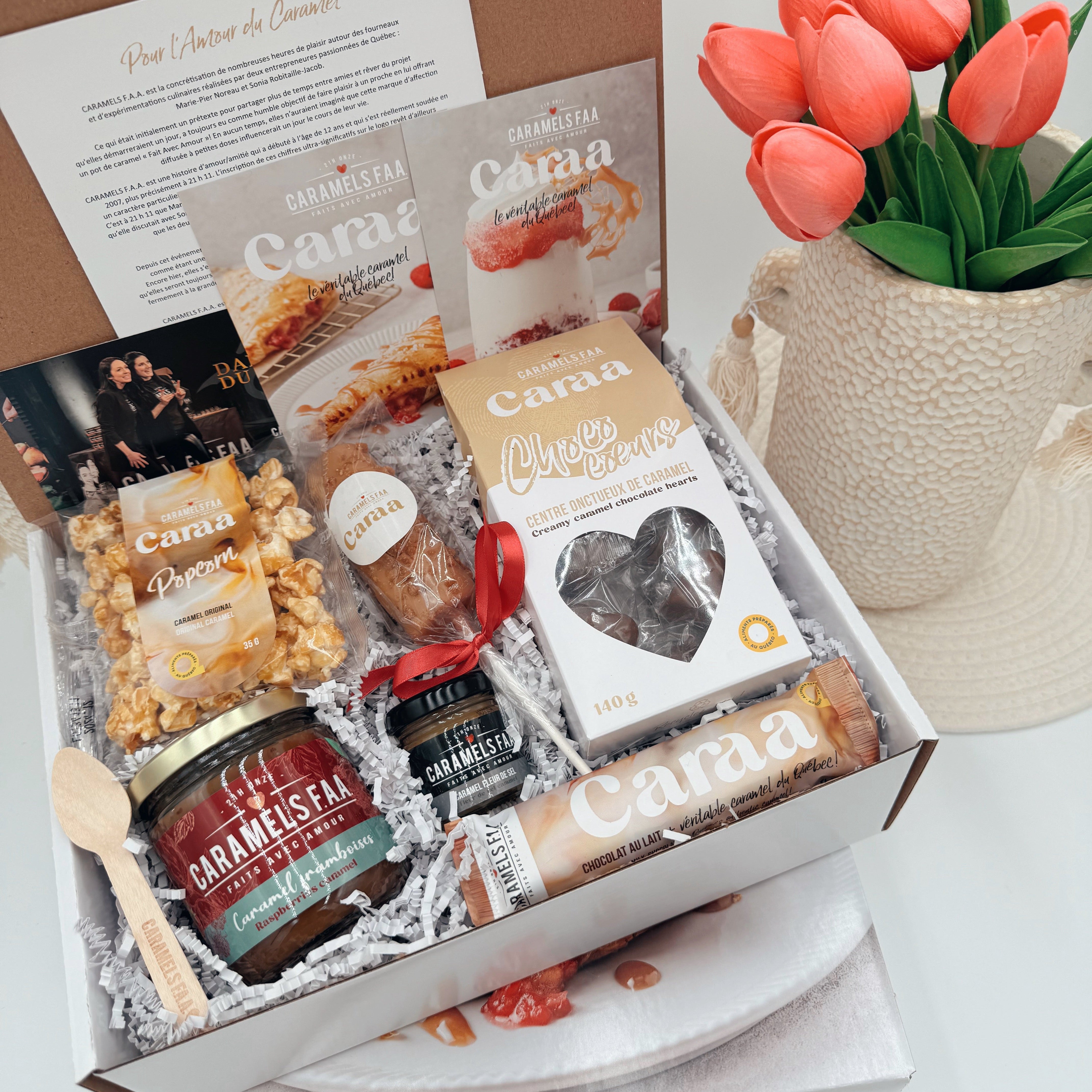 Gift box with Cama products including cheese, jam, and other snacks, accompanied by a vase of tulips.