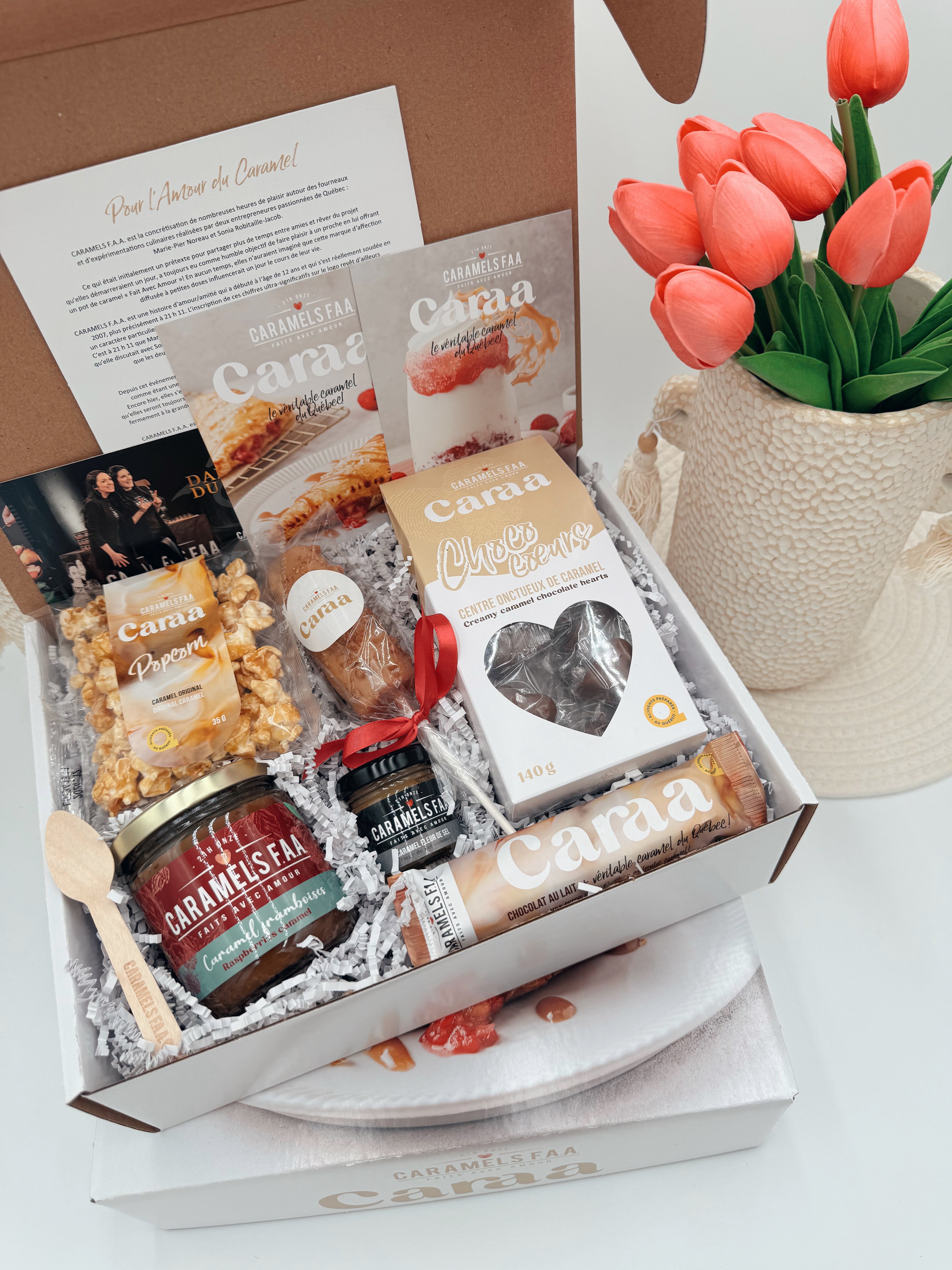 Gift box with Cama products including cheese, jam, and other snacks, accompanied by a vase of tulips.