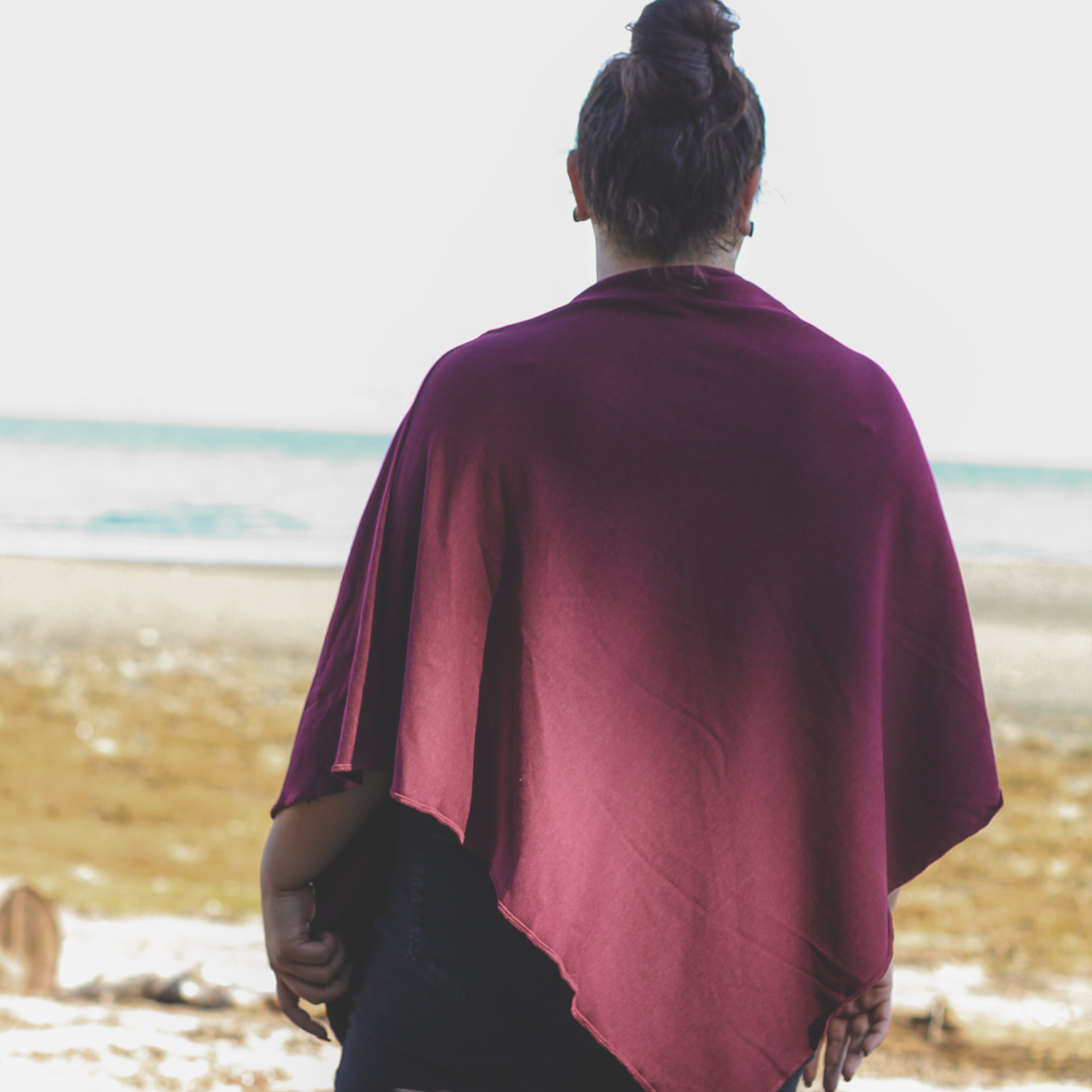 Person wearing a burgundy poncho standing on a beach