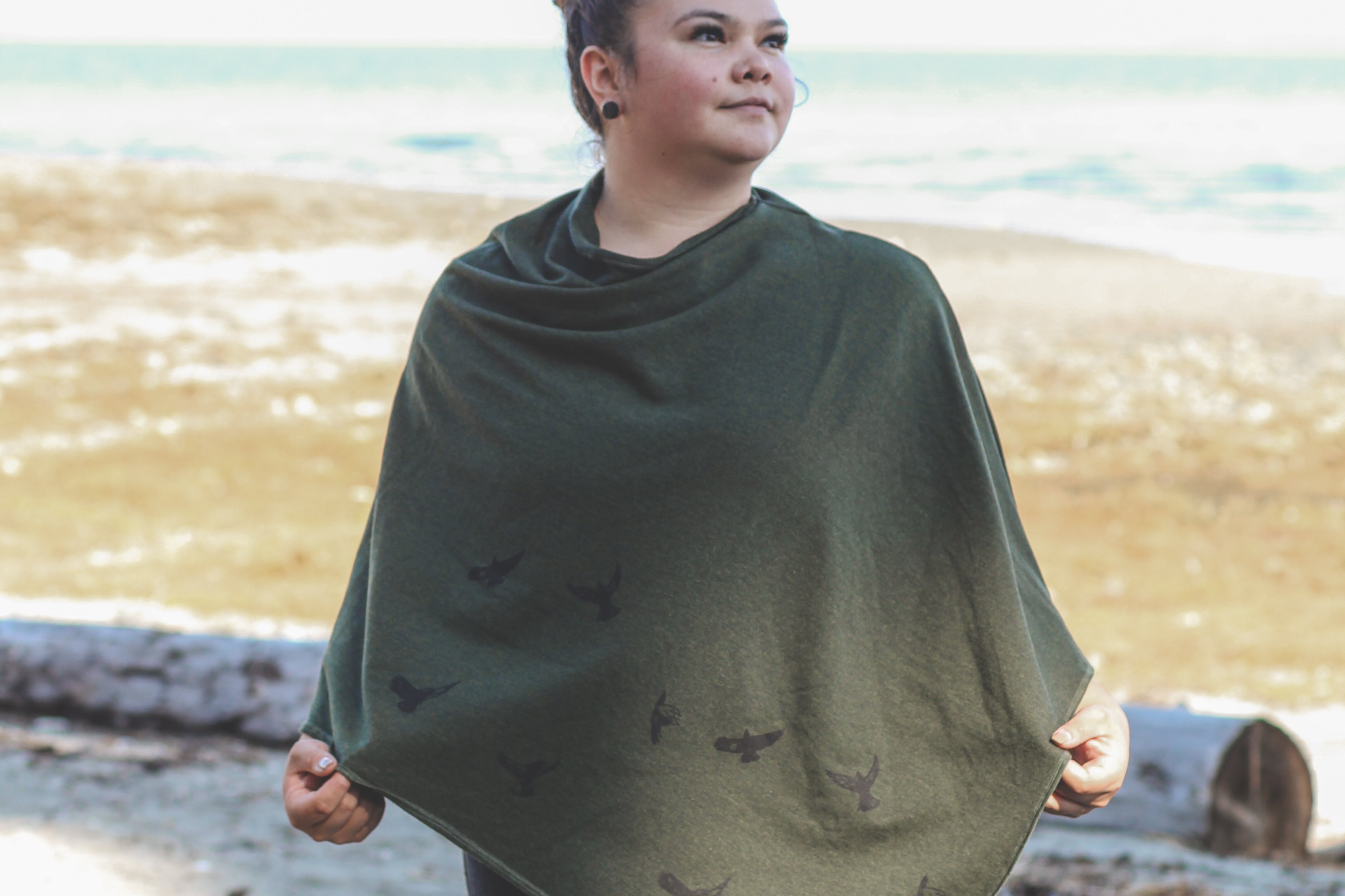 Woman wearing a green poncho on a beach with ocean in the background