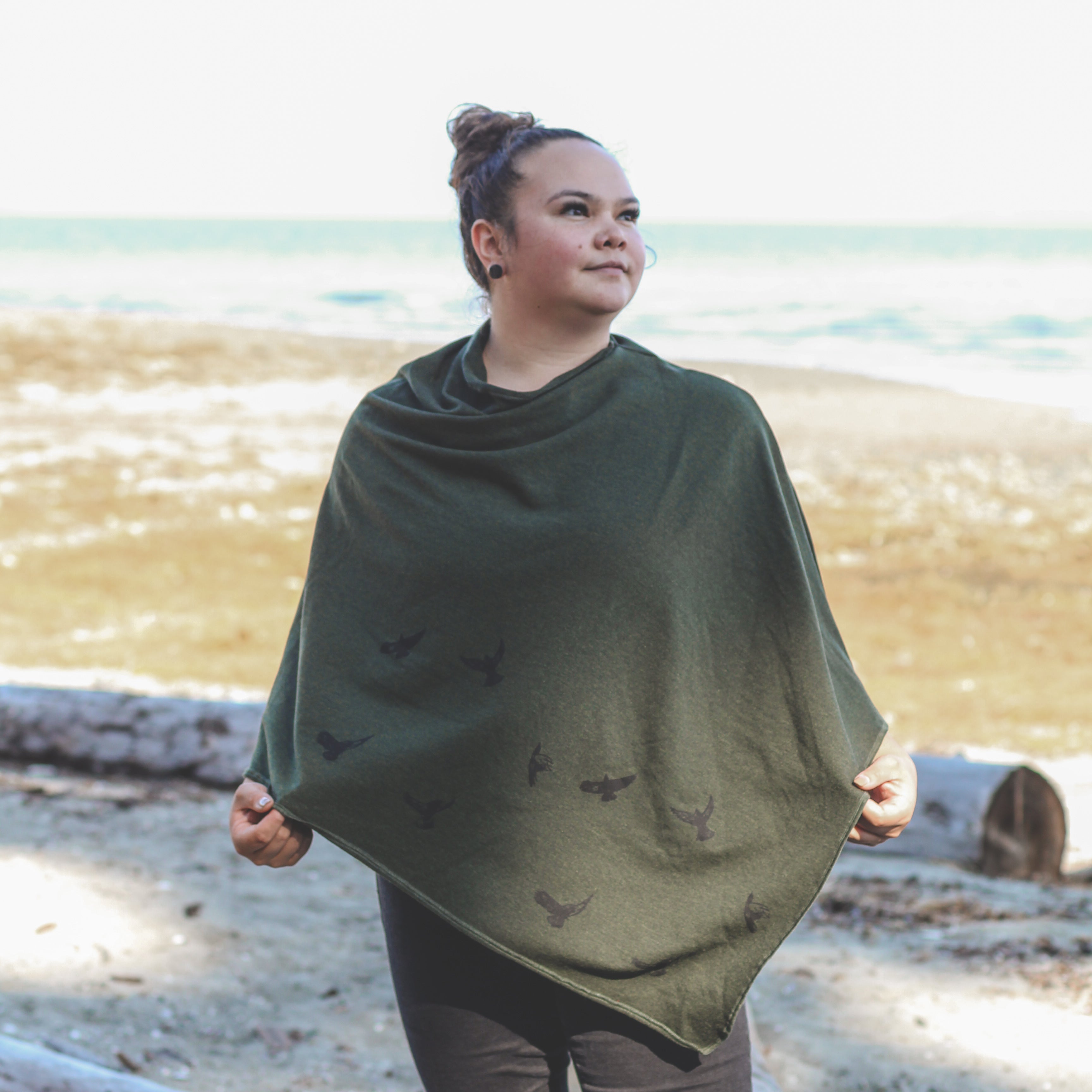 Woman wearing a green poncho on a beach with ocean in the background