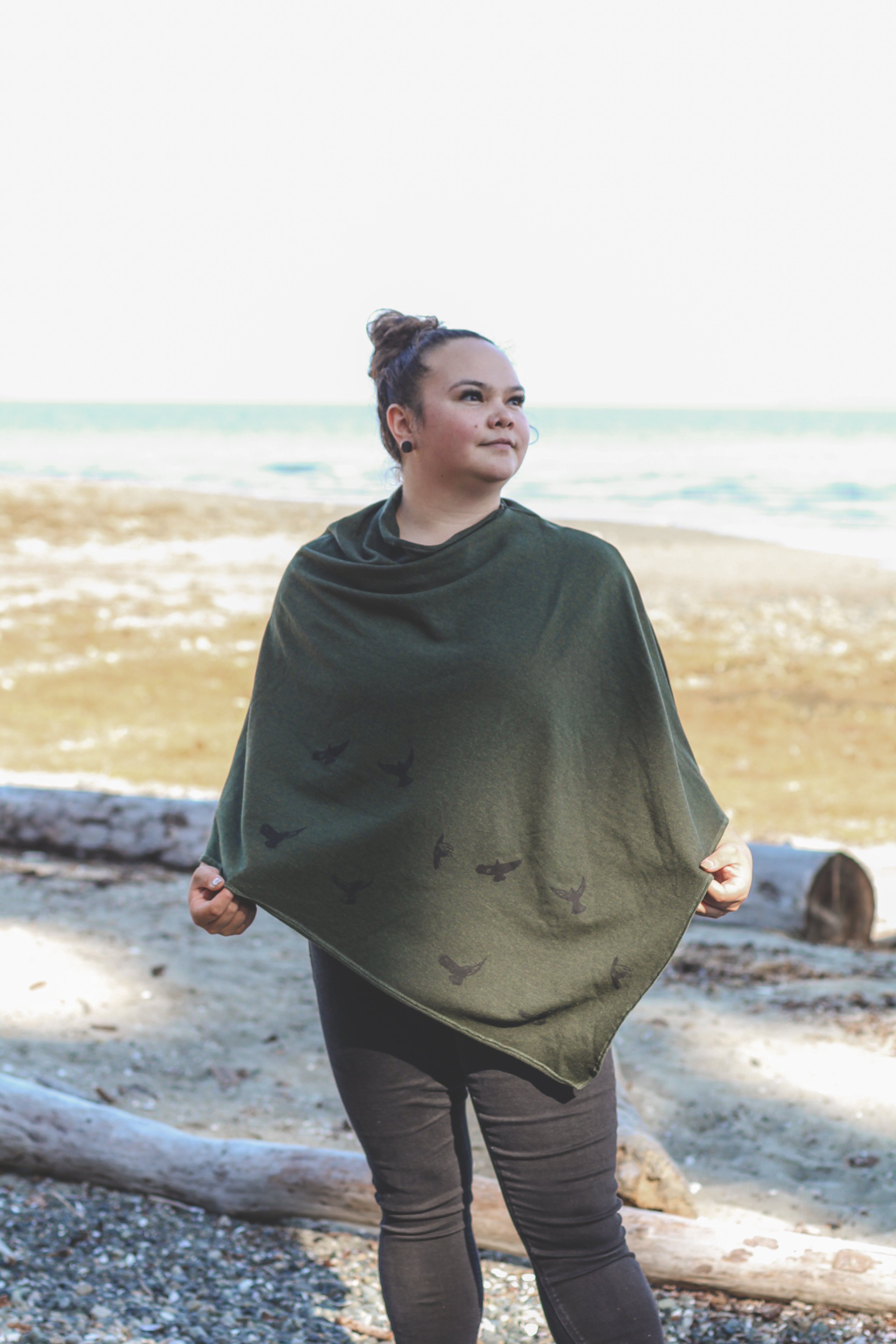 Woman wearing a green poncho on a beach with ocean in the background