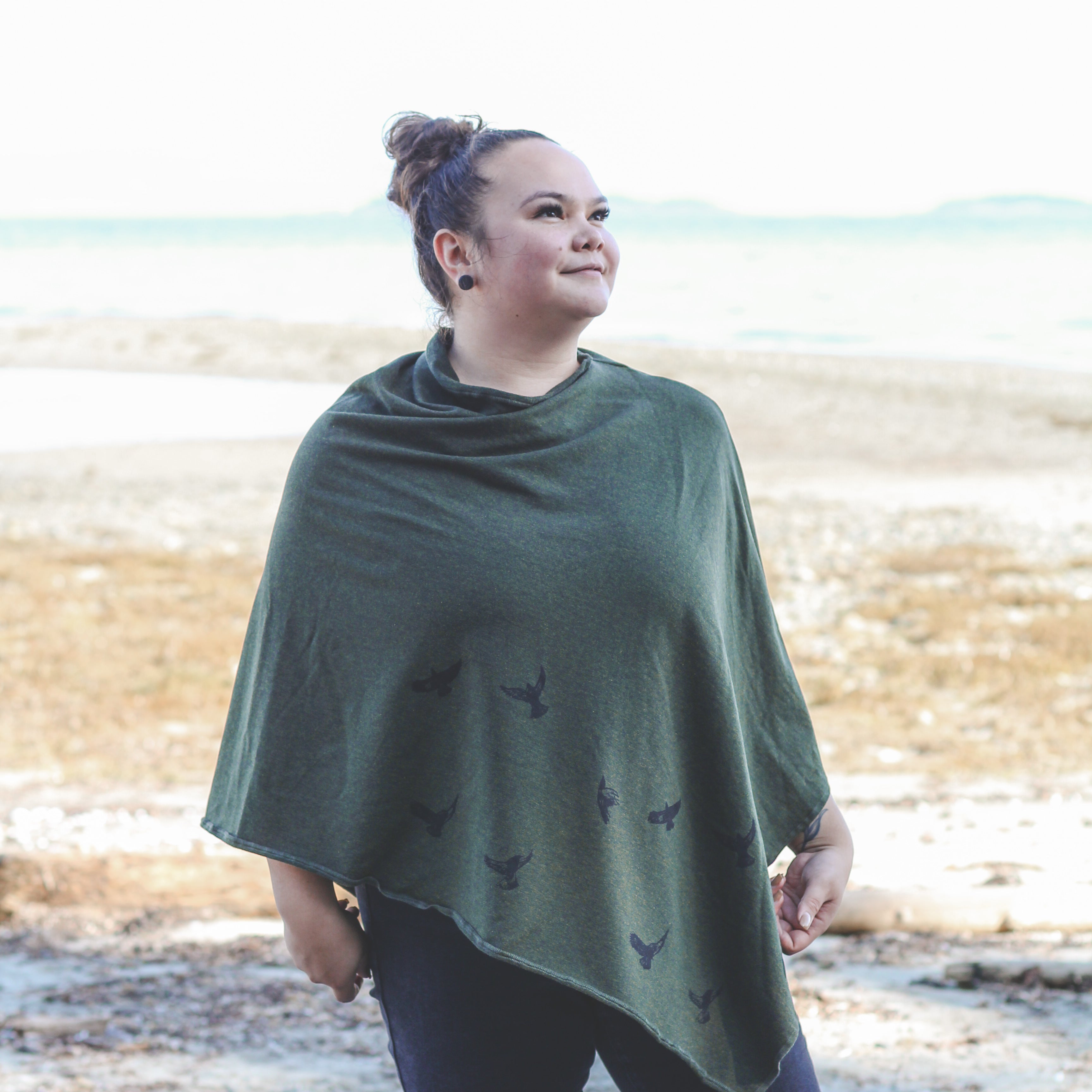 Woman wearing a green poncho with bird patterns standing on a beach.
