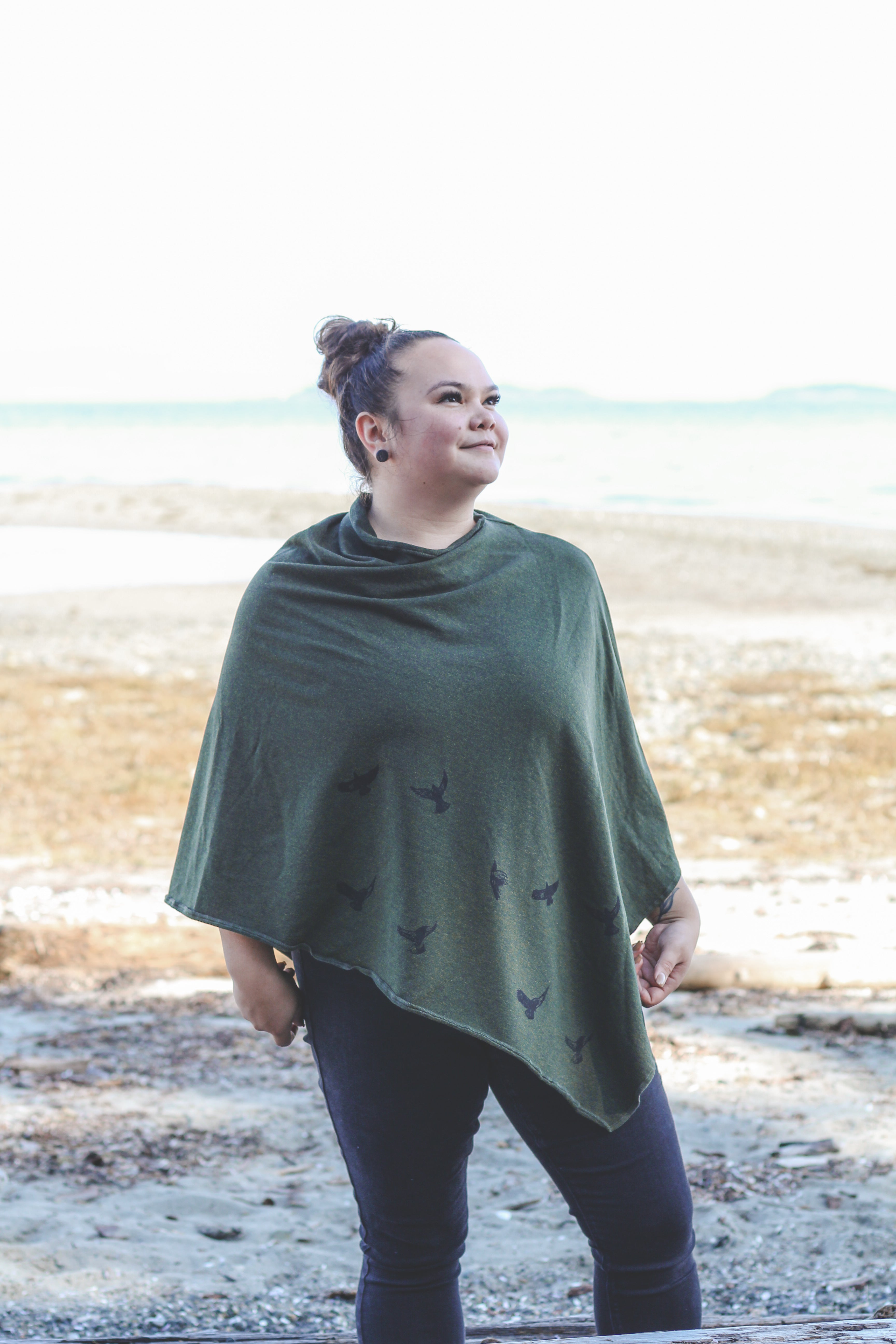 Woman wearing a green poncho with bird patterns standing on a beach.