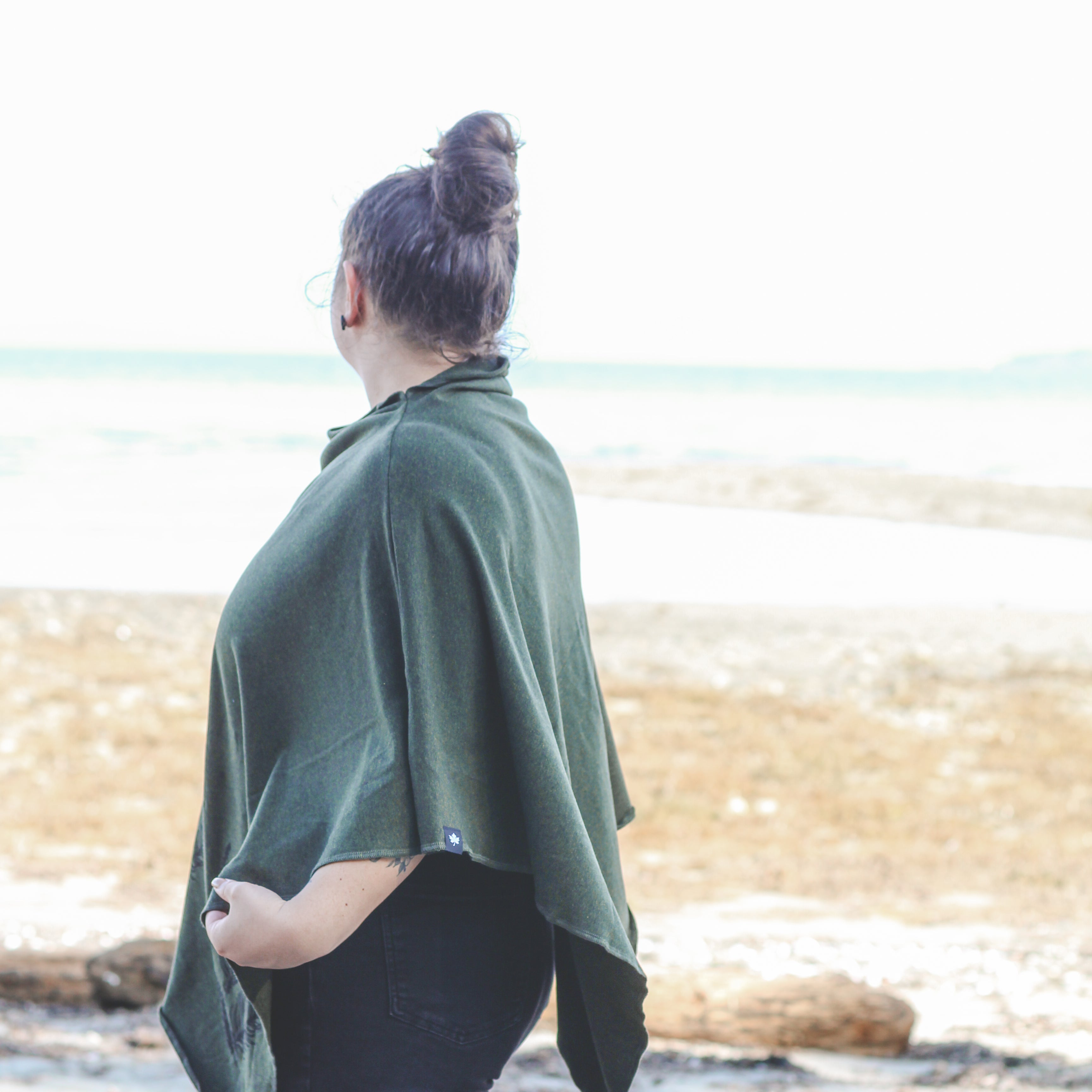 Person wearing a green poncho standing on a beach with ocean in the background