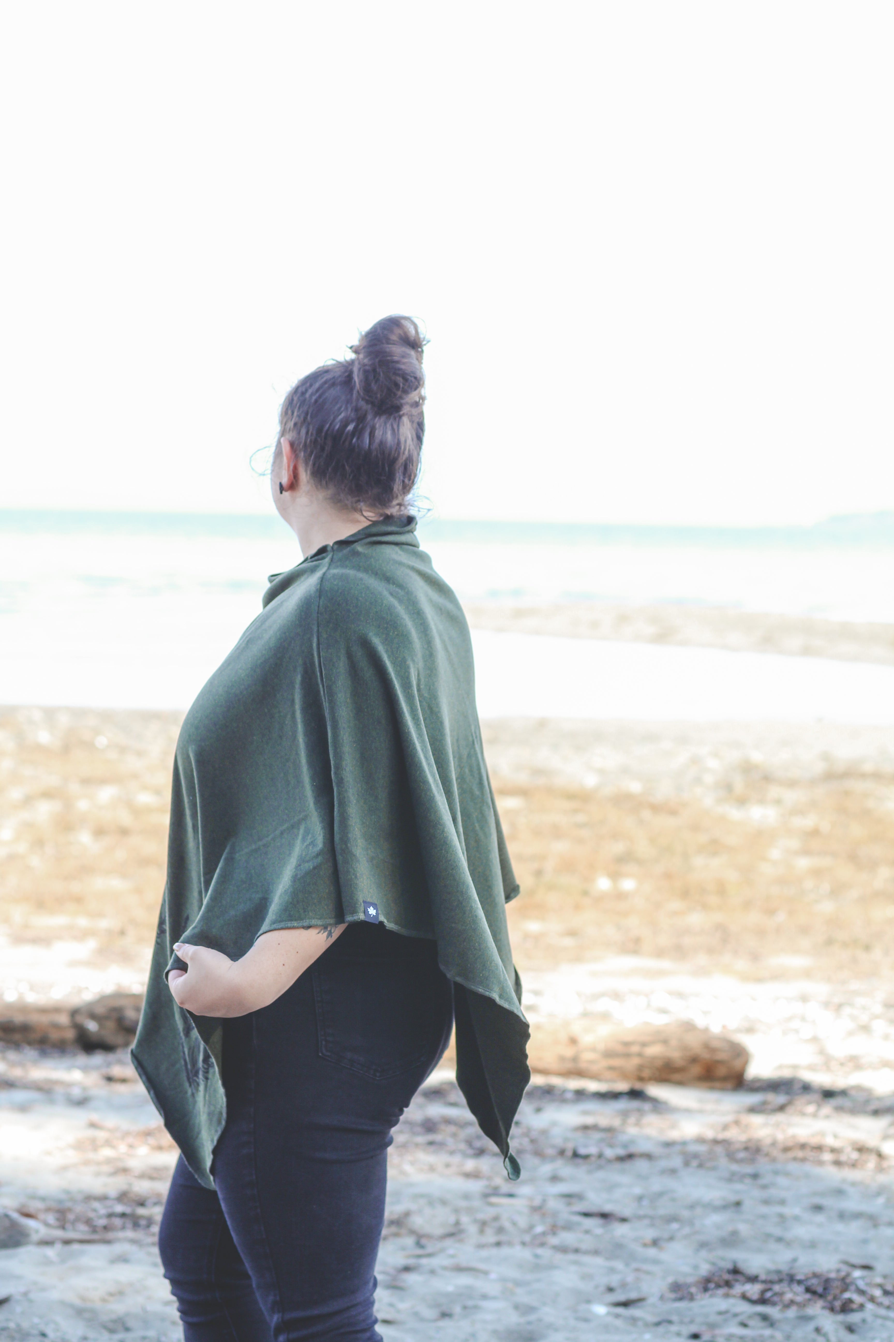 Person wearing a green poncho standing on a beach with ocean in the background