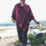 Person wearing a maroon poncho walking on a log in a natural setting