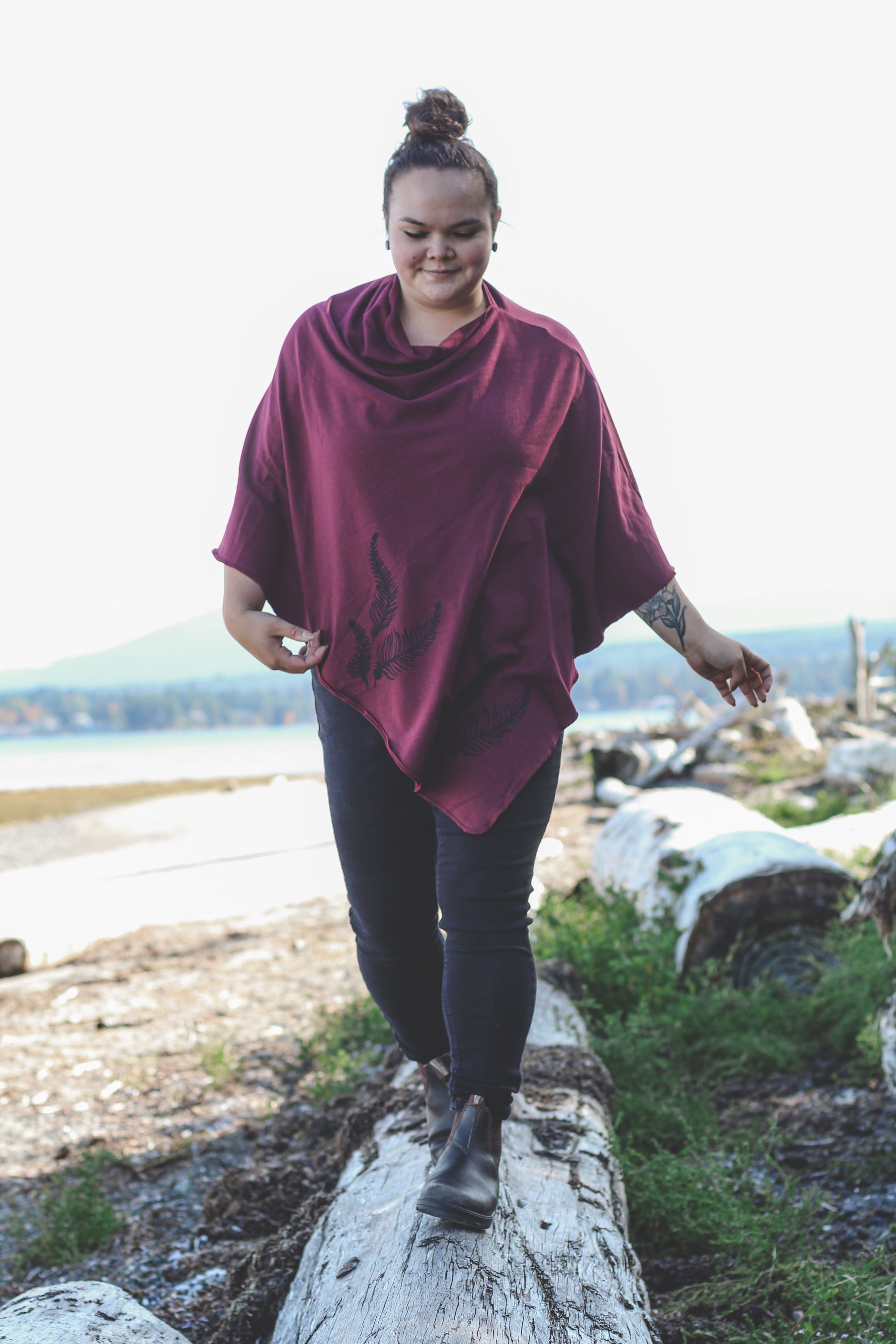 Person wearing a maroon poncho walking on a log in a natural setting
