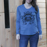 Woman wearing a blue long-sleeve shirt with a graphic design in front of a wooden wall.