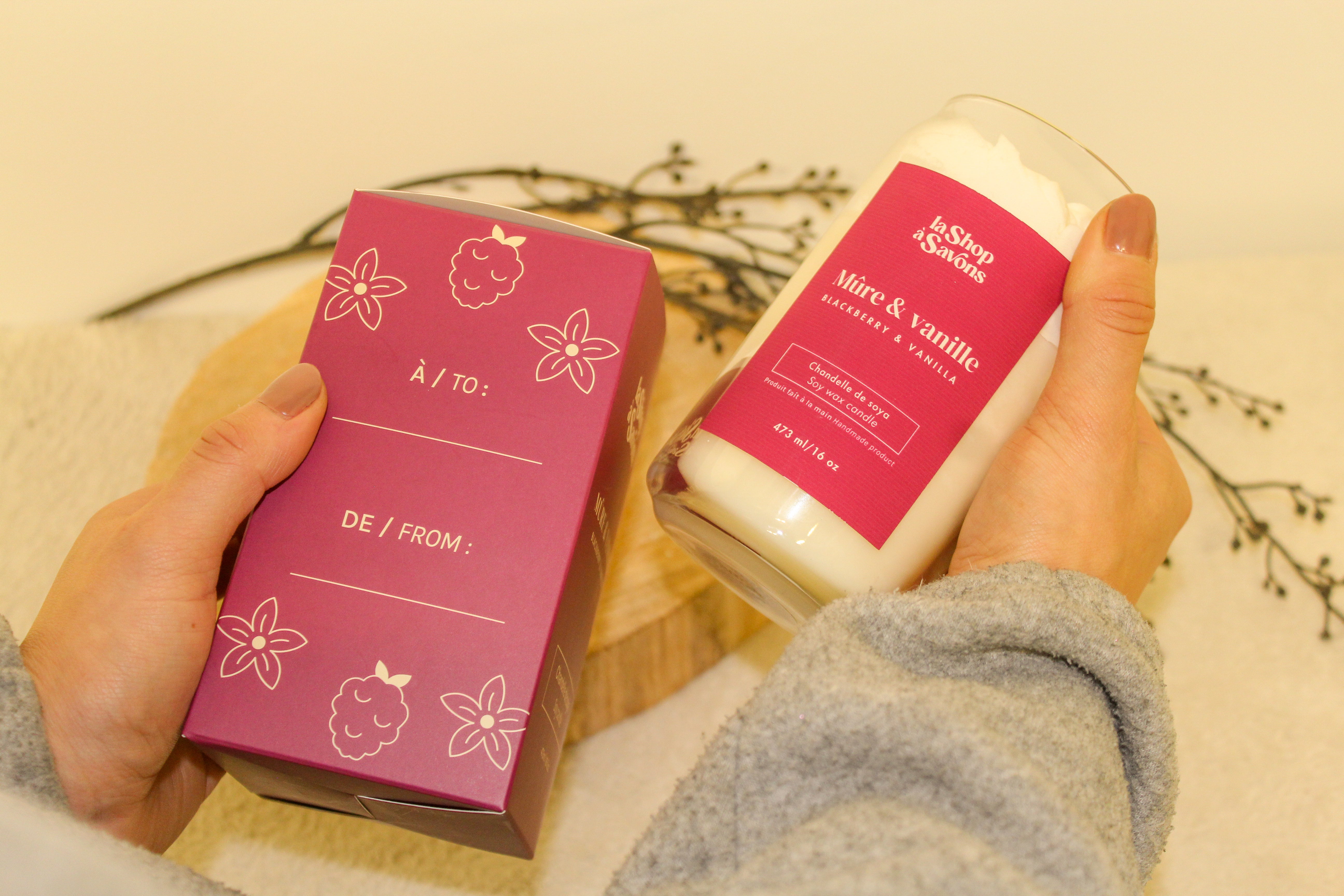 Two products with pink packaging held by hands against a neutral background