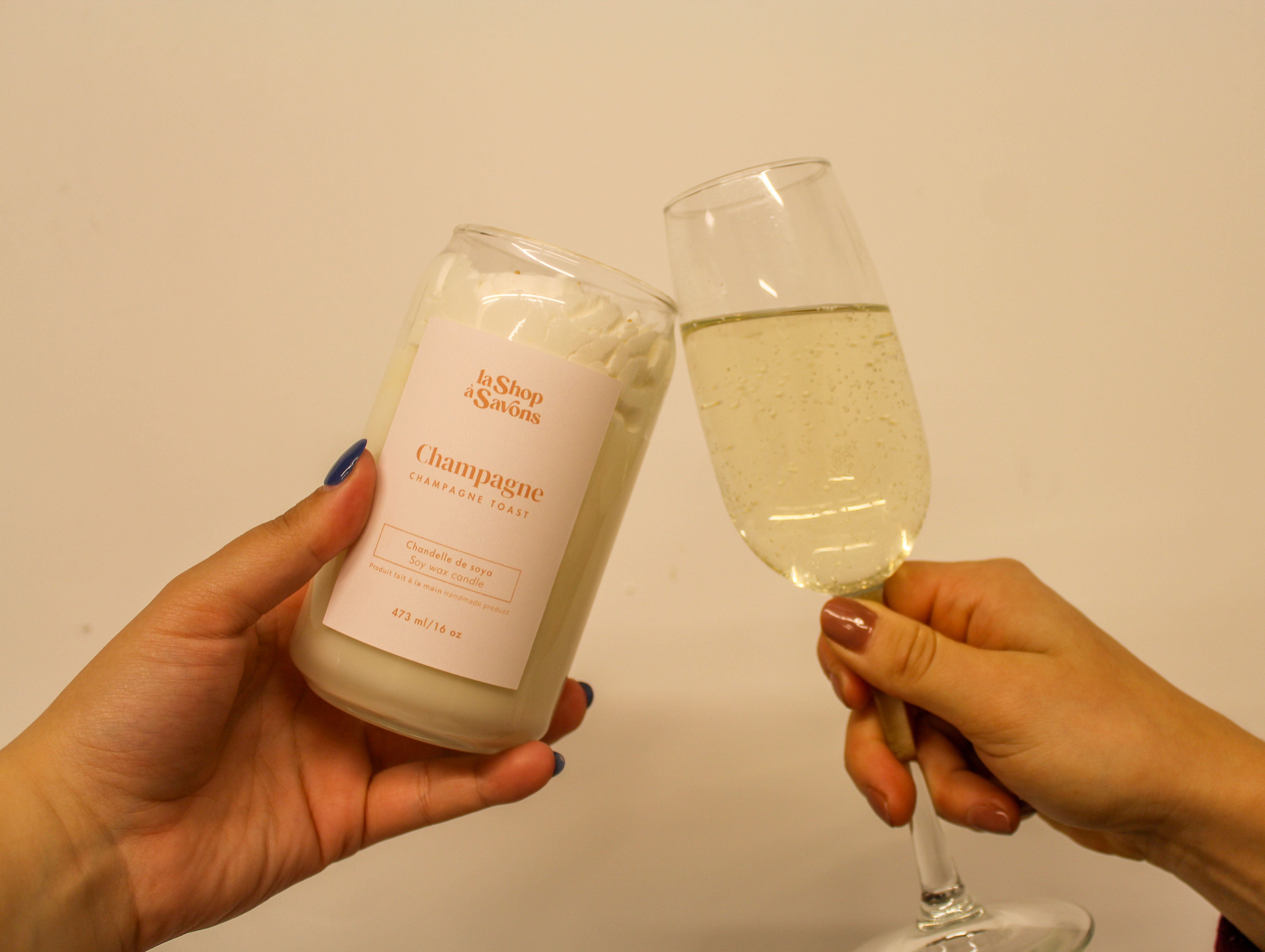 Two hands holding a bottle labeled 'Champagne' and a glass filled with a bubbly liquid against a plain background.