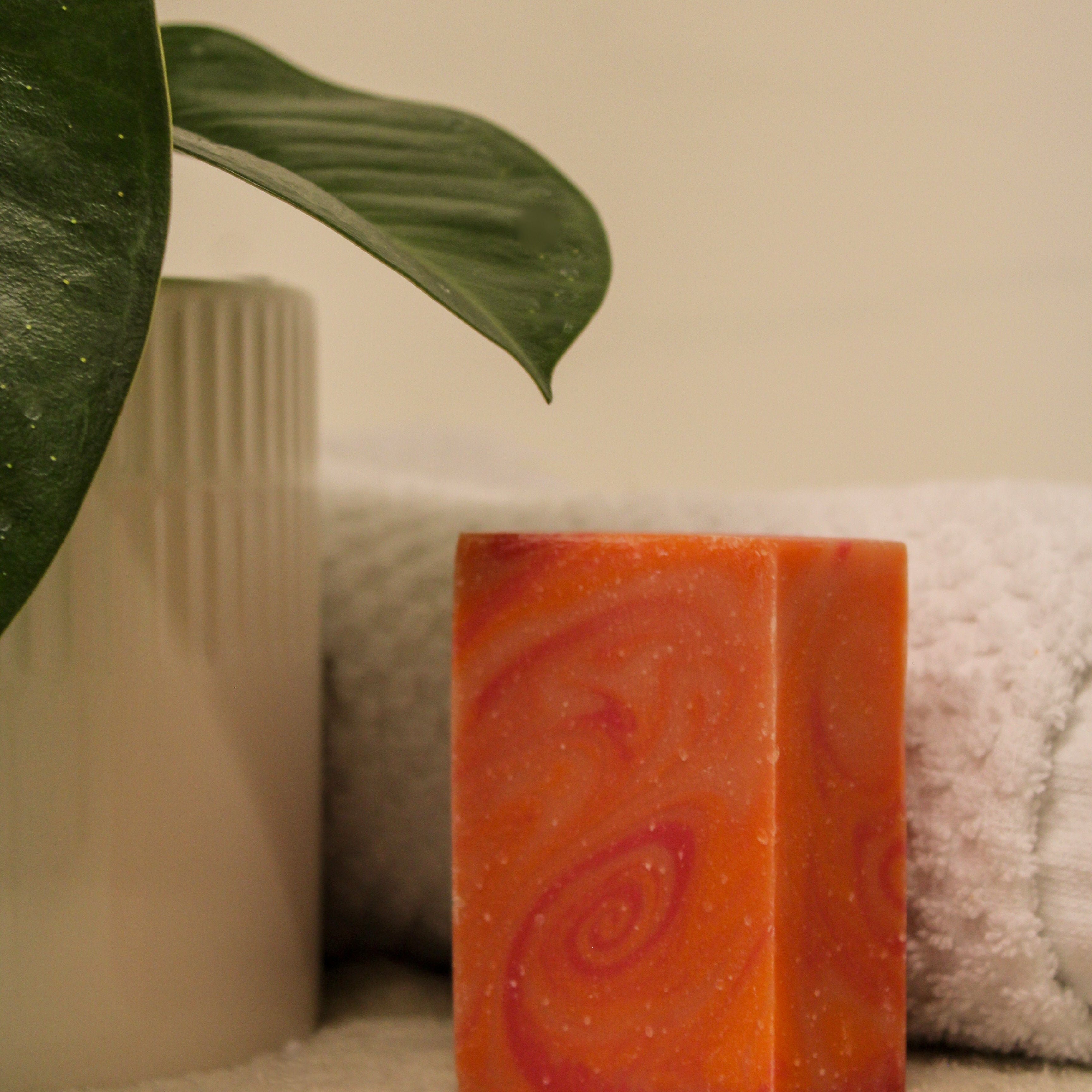 Orange soap bar with a spiral design on a towel next to a plant