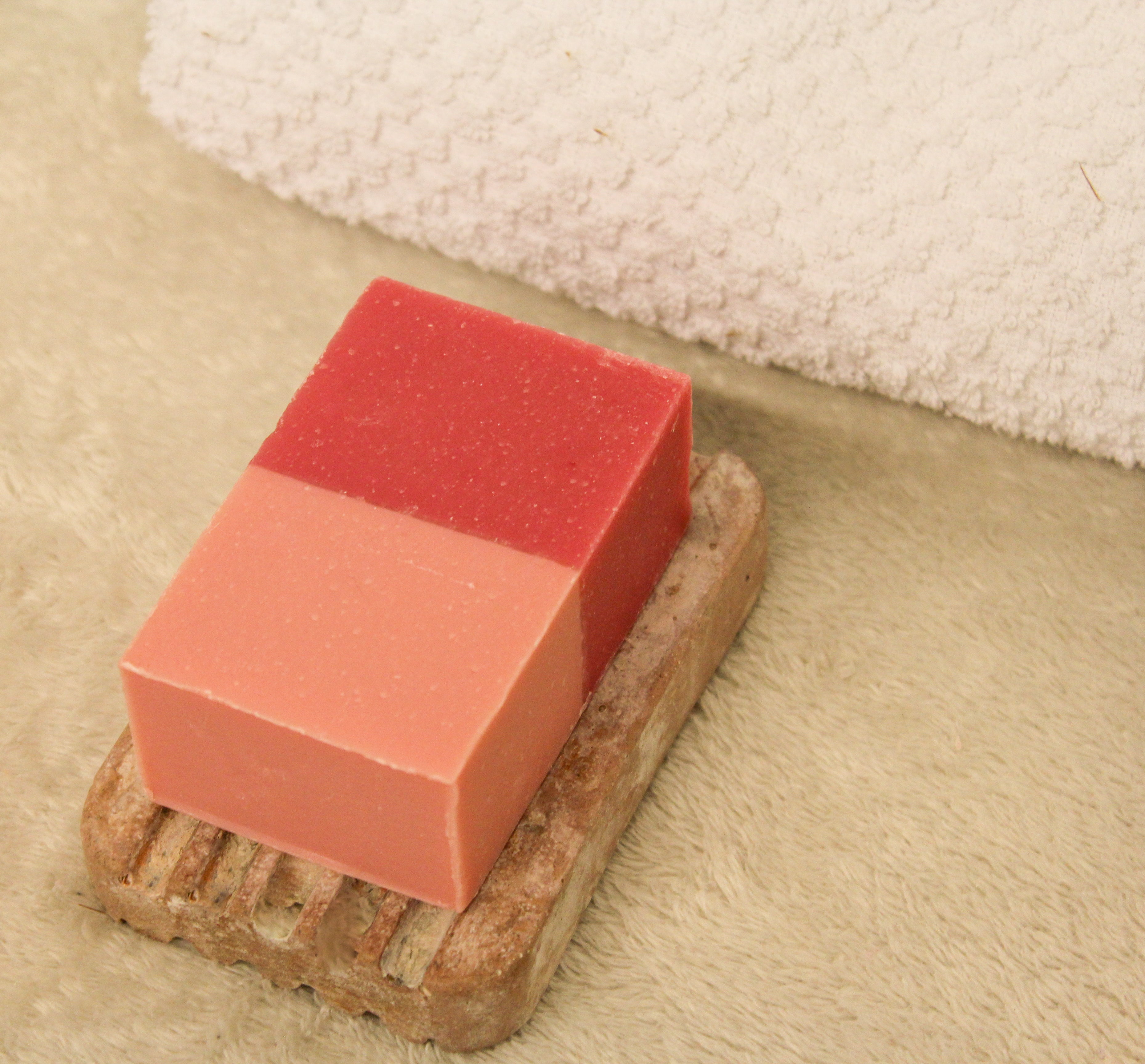Red and pink soap bar on a stone soap dish with a white towel in the background.