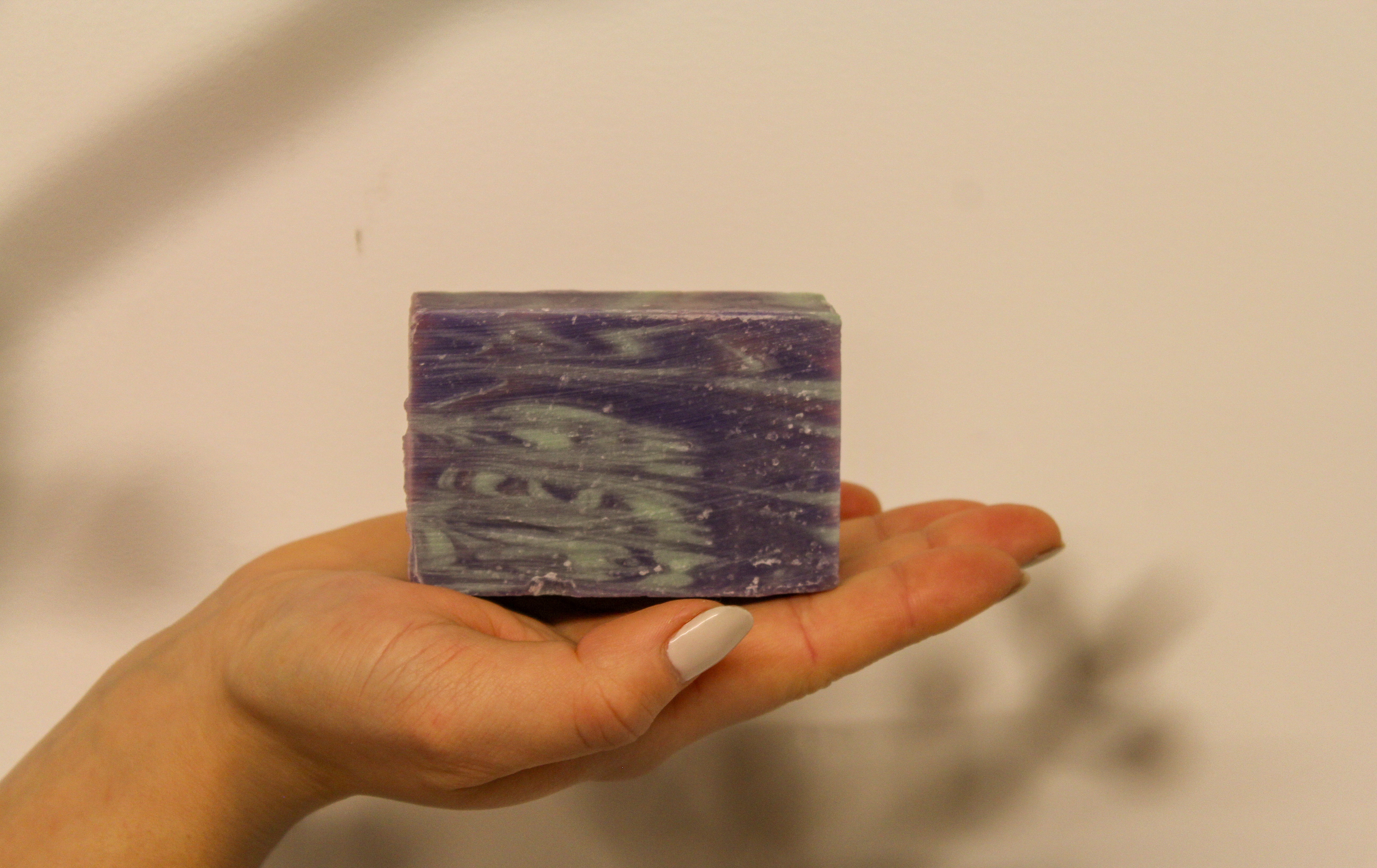 Hand holding a bar of purple soap against a plain background