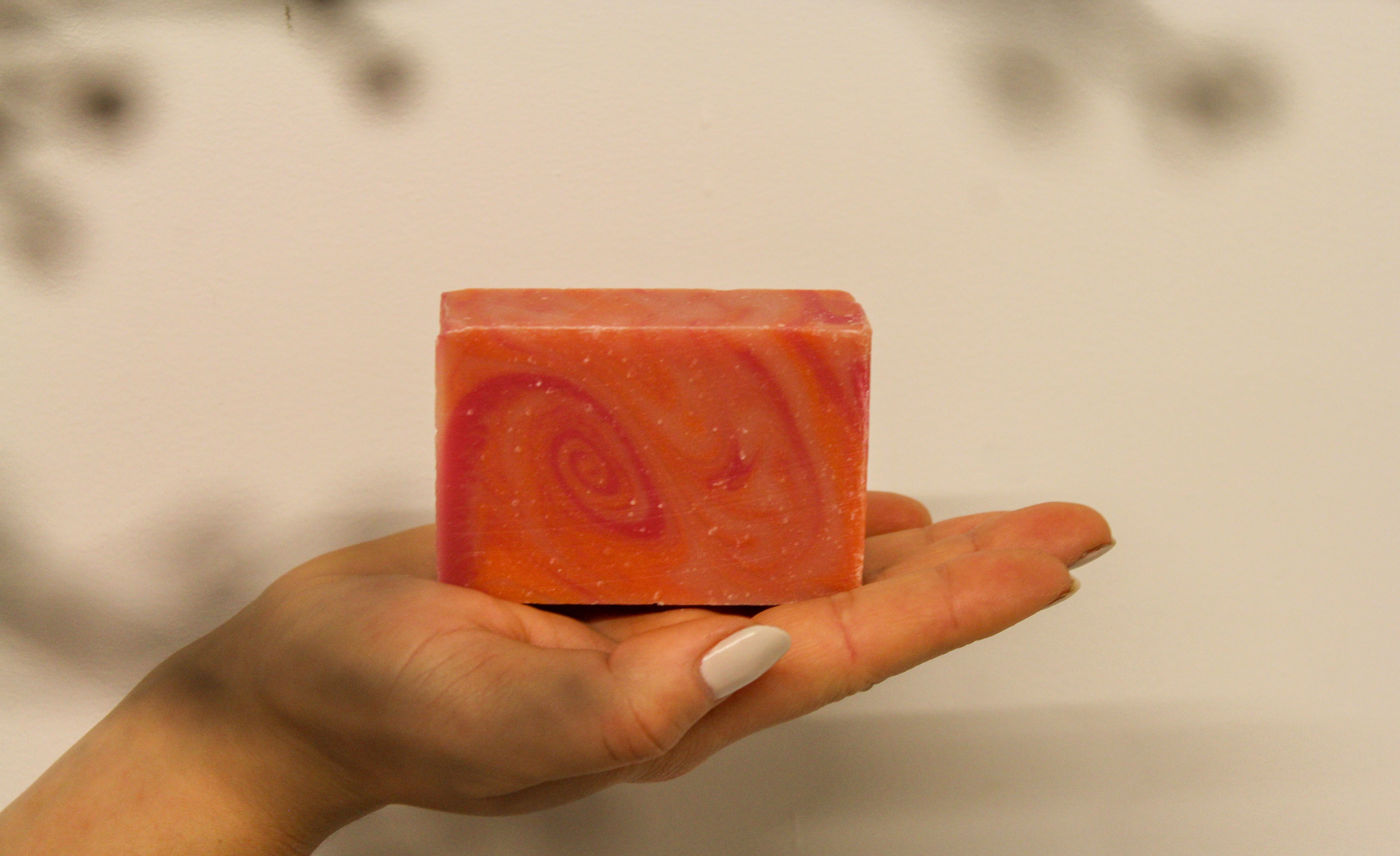 Hand holding a red soap bar with a spiral pattern against a blurred background