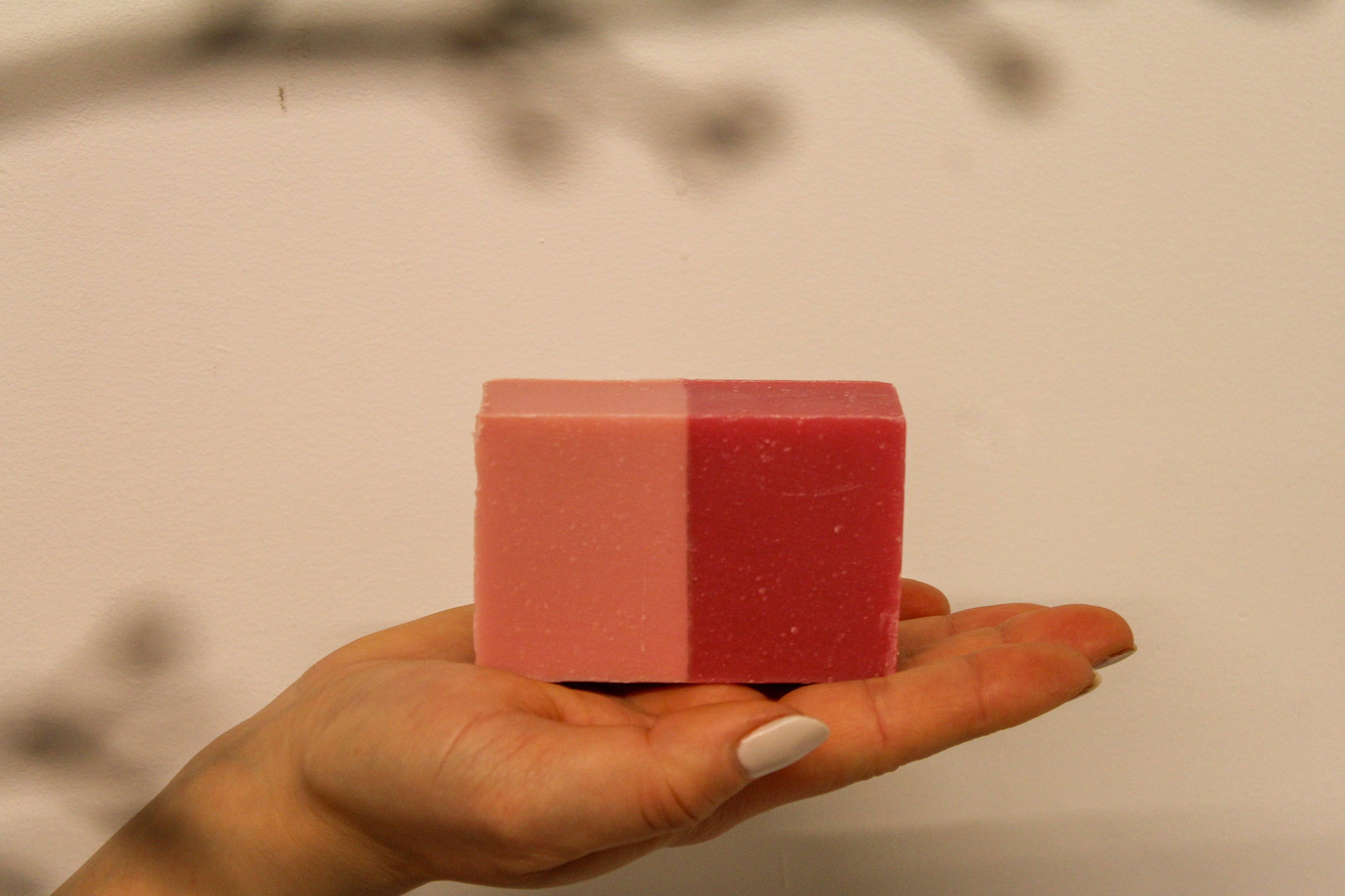 Hand holding a pink and red striped bar of soap against a neutral background