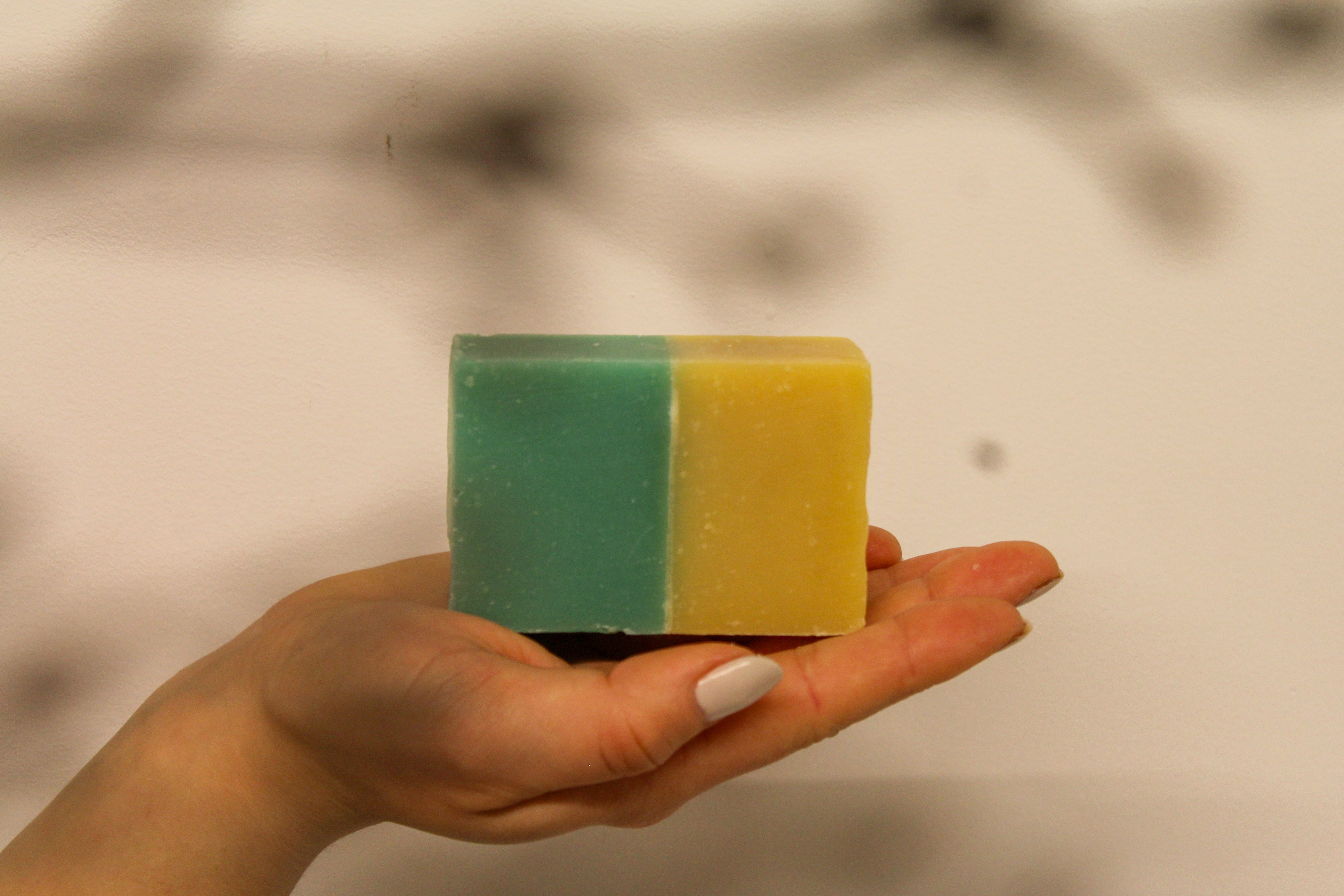 Hand holding a two-tone green and yellow soap bar against a blurred background