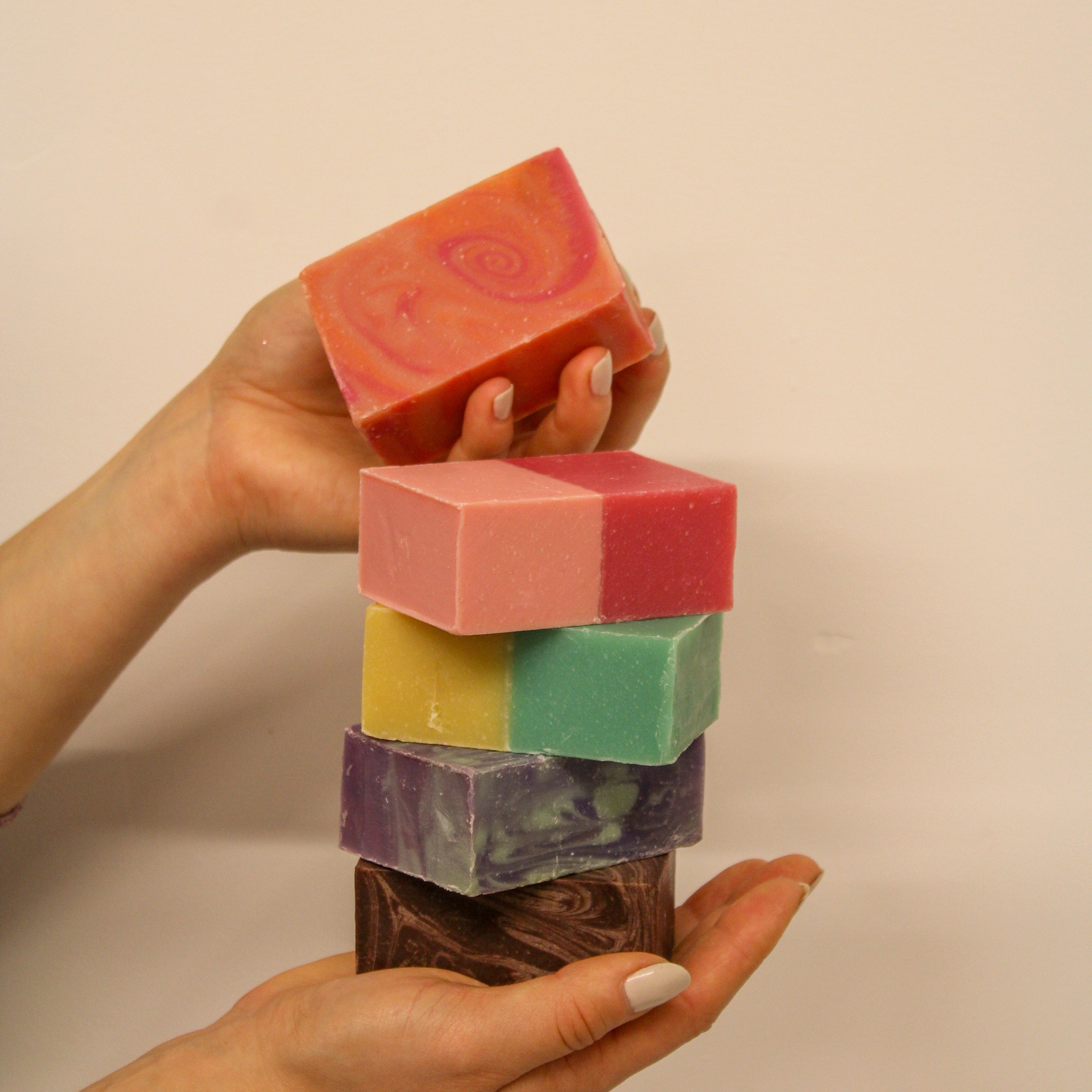 Hand holding a stack of colorful soap bars against a beige background