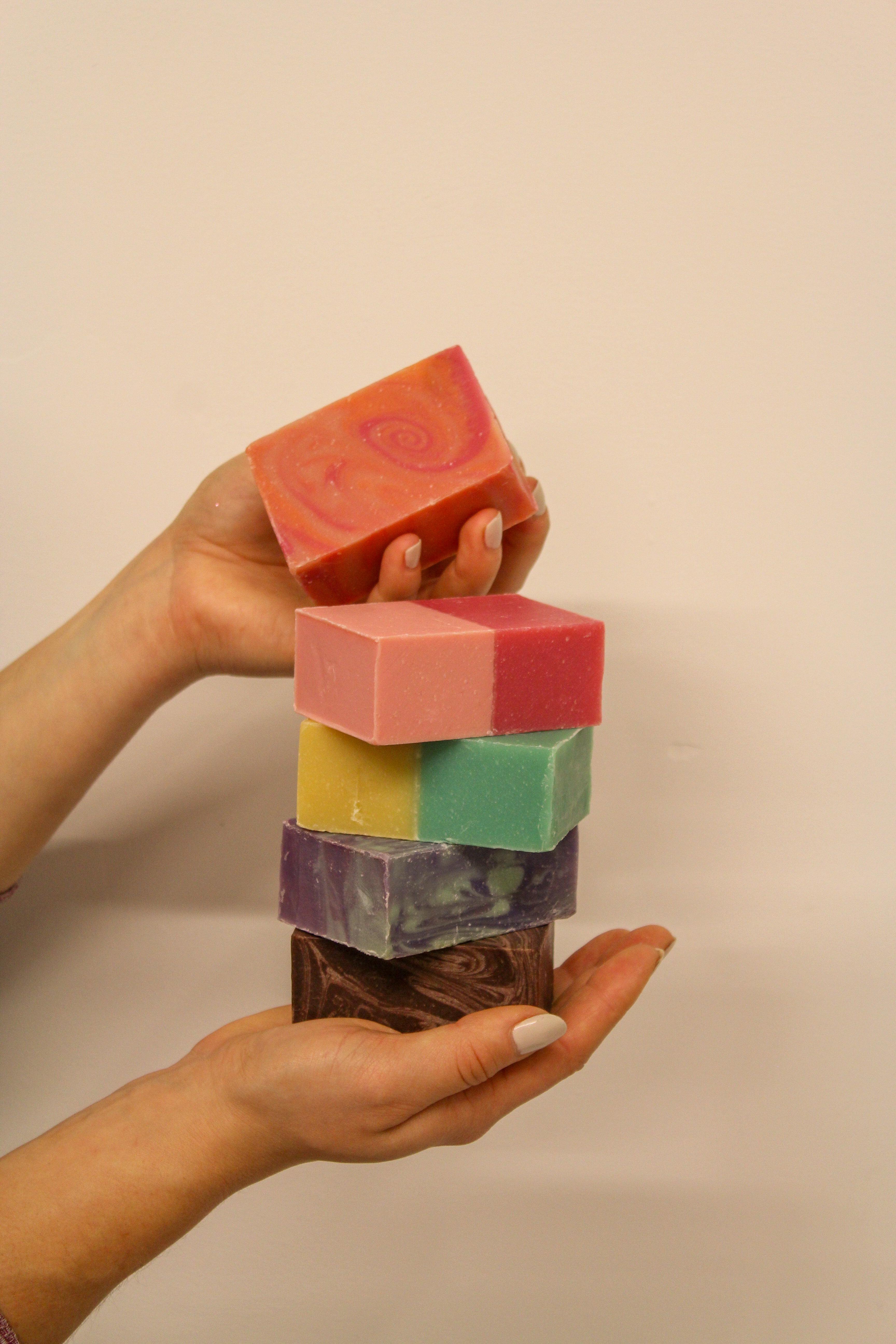 Hand holding a stack of colorful soap bars against a beige background