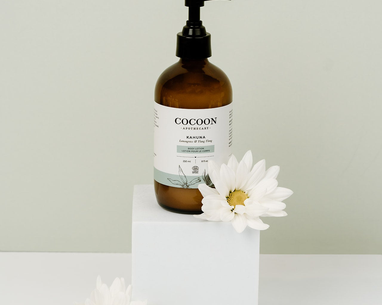 Brown bottle labeled 'Cocoon' with a white label on a white surface with white flowers.