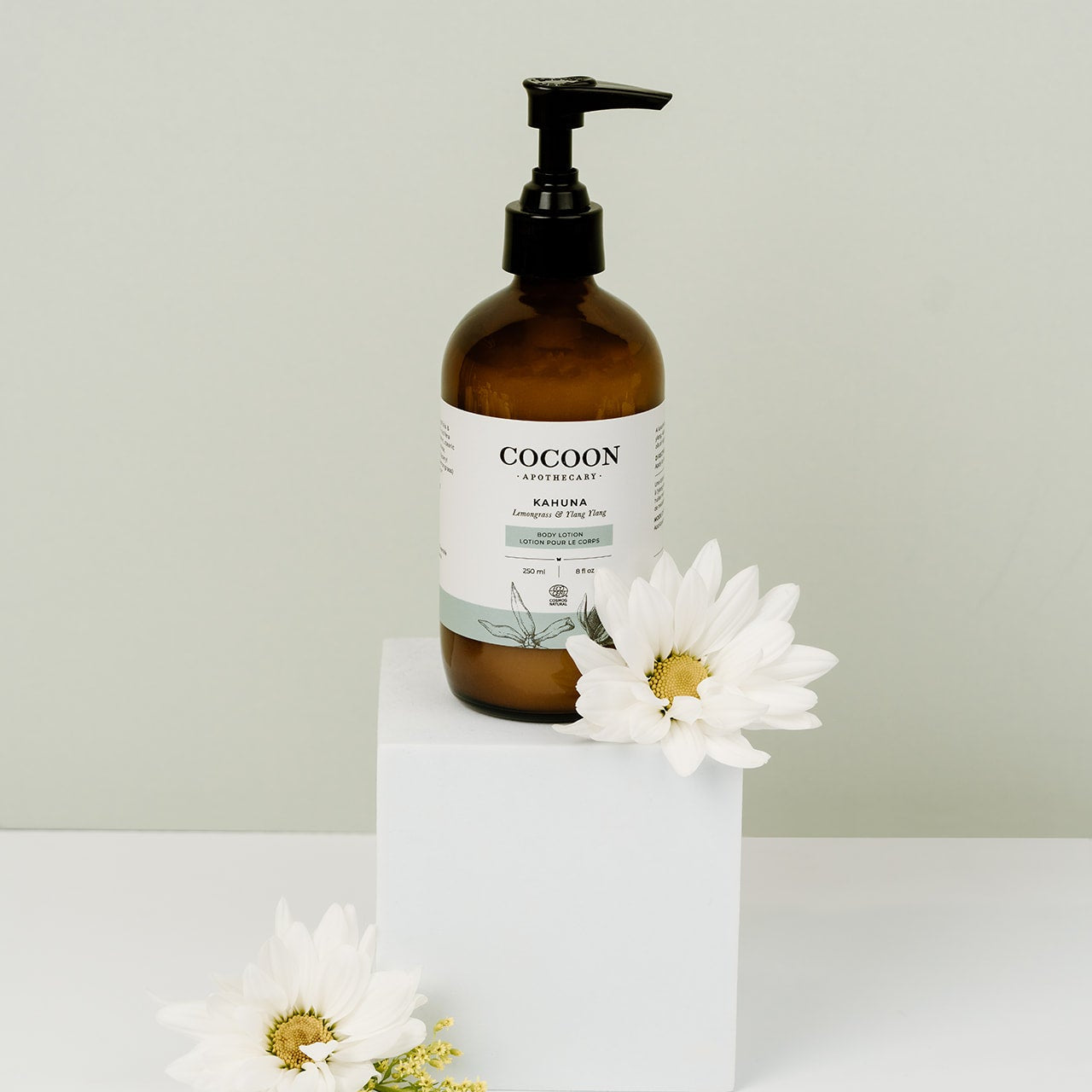 Brown bottle labeled 'Cocoon' with a white label on a white surface with white flowers.