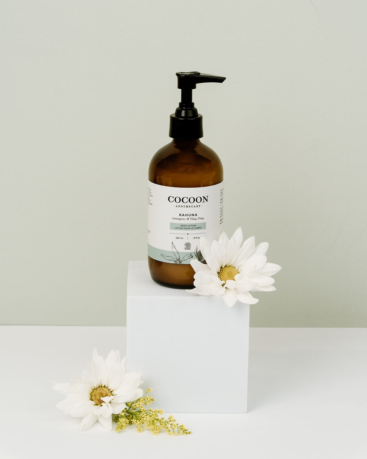 Brown bottle labeled 'Cocoon' with a white label on a white surface with white flowers.