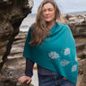 Woman wearing a teal poncho with leaf patterns by a rocky coastal area